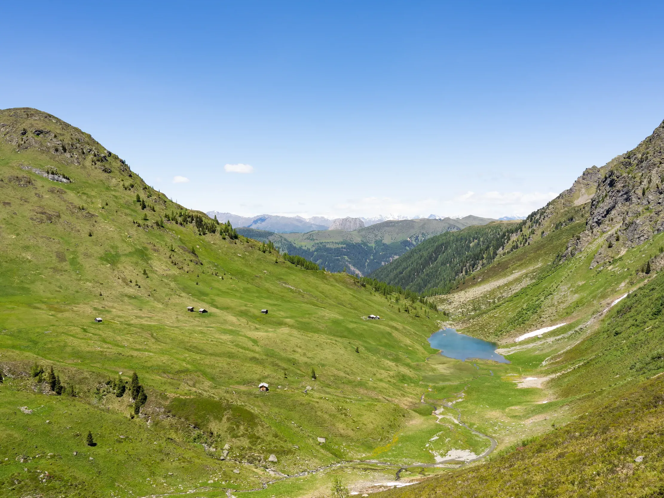 Weitblick über ein sonniges, grünes Almhochtal mit einem kleinen Bergsee auf dem Karnischen Höhenweg in den Alpen.