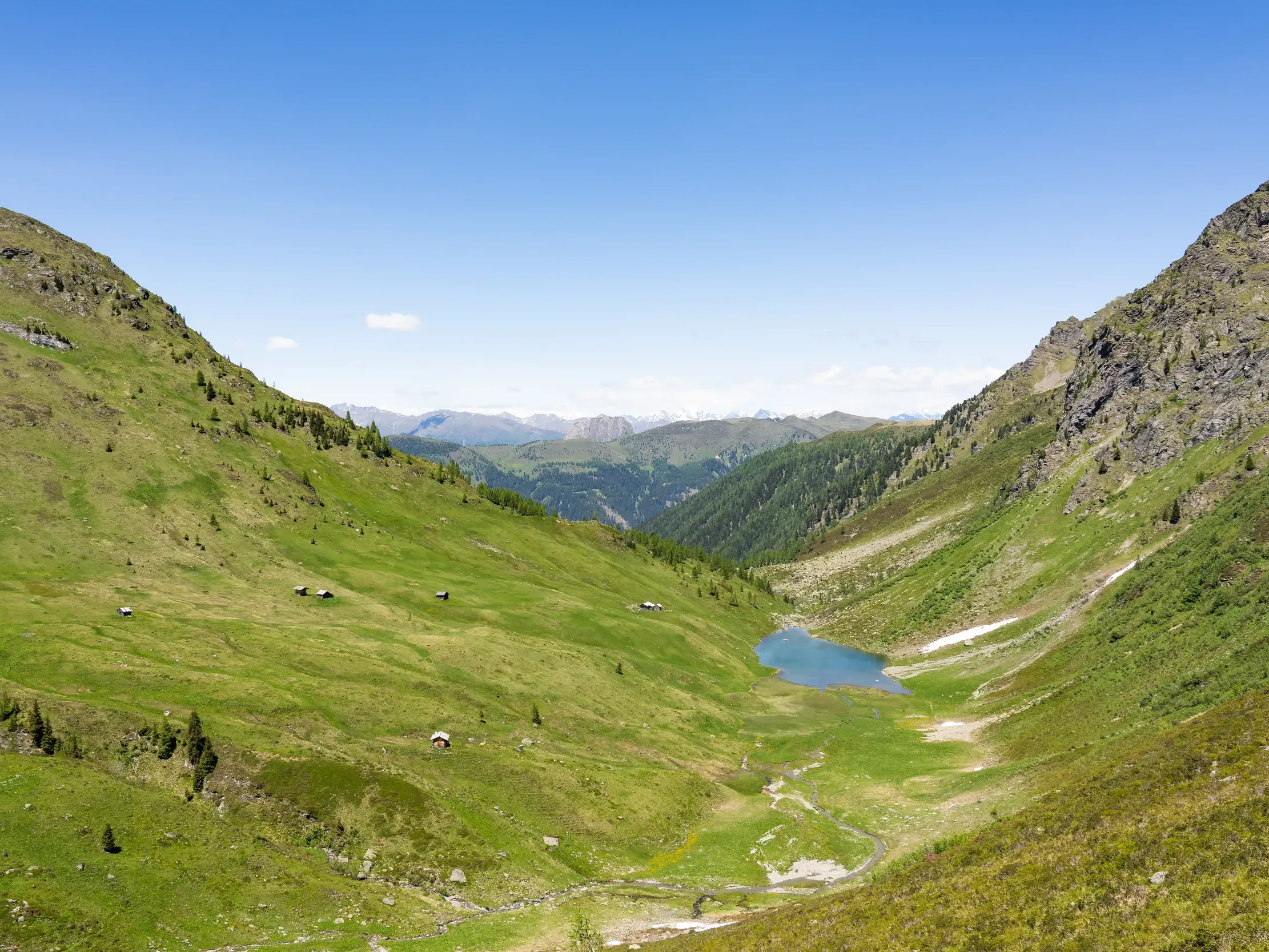 Sonniges Alpental mit einem klaren Bergsee und grünen Almwiesen auf dem Karnischen Höhenweg in den Karnischen Alpen.
