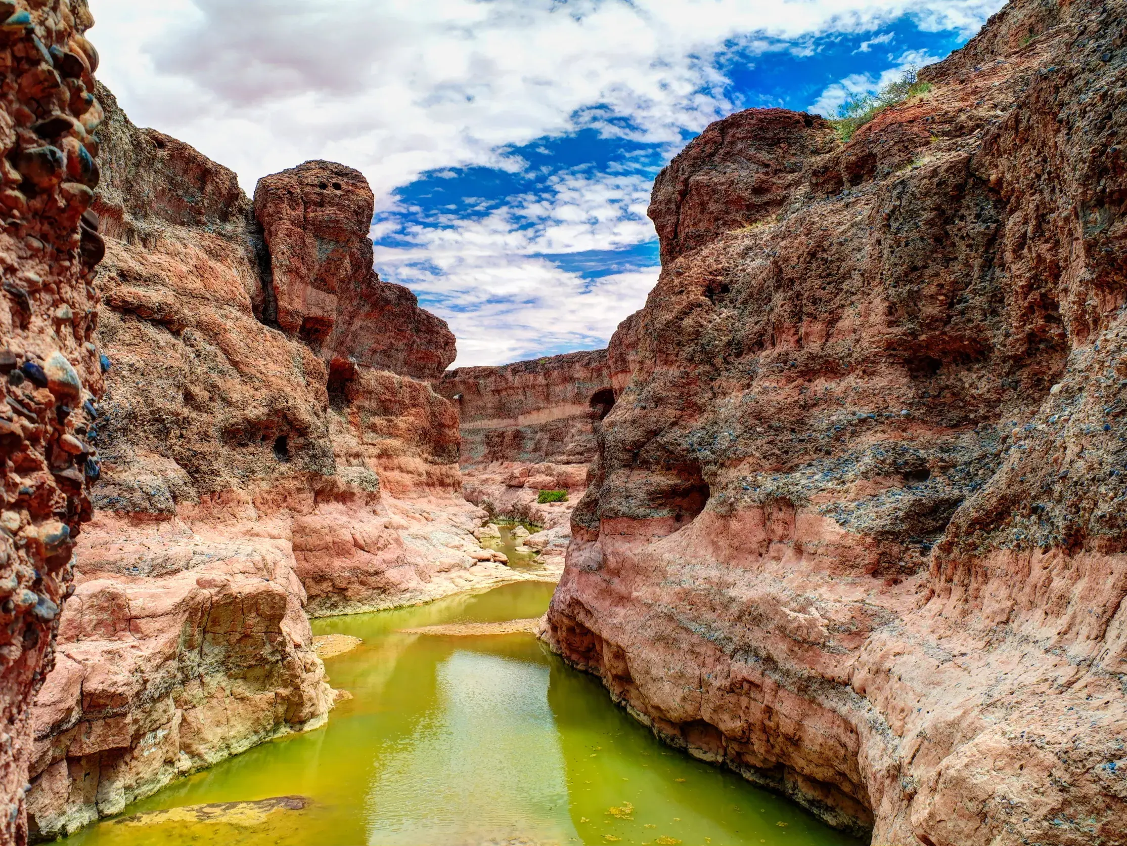 Enge, rotsandige Schlucht des Sesriem-Canyons in Namibia, durch die sich ein grünes Gewässer schlängelt.