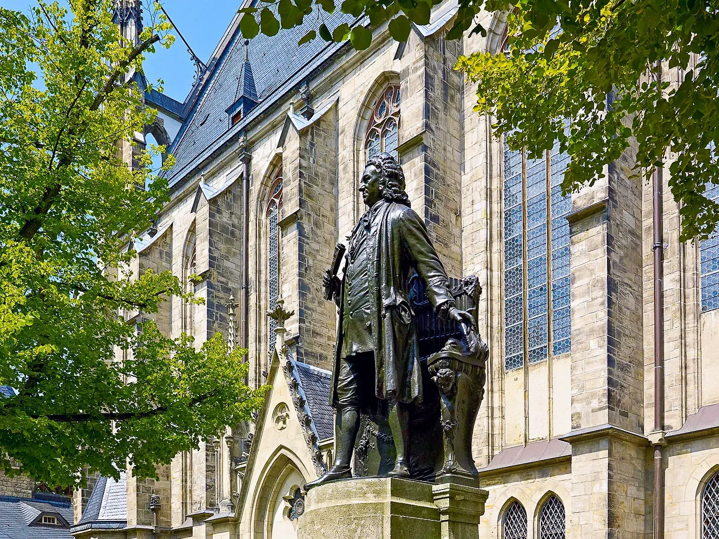 Bronzenes Johann-Sebastian-Bach-Denkmal vor den gotischen Bogenfenstern der Thomaskirche in Leipzig.