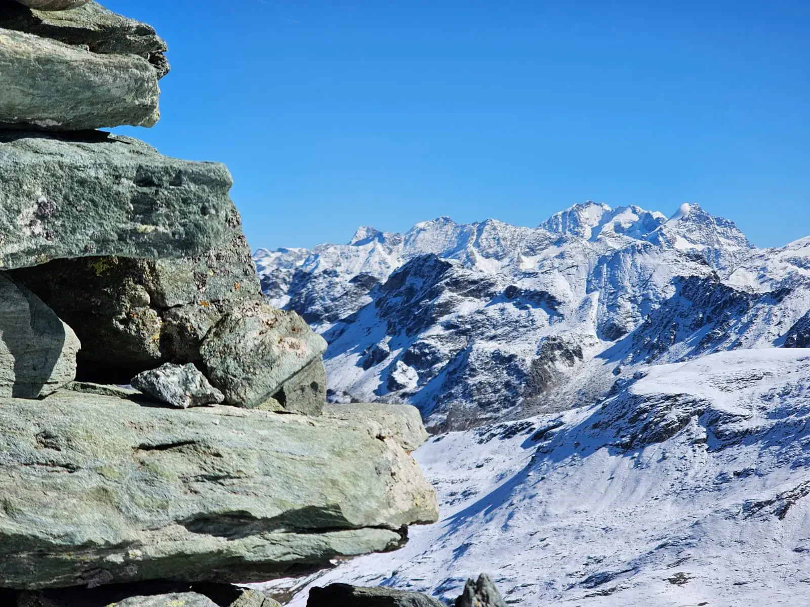 Ein Steinmann auf einem Bergpass in Graubünden mit weitem Panoramablick auf die schneebedeckten Gipfel der Alpen.