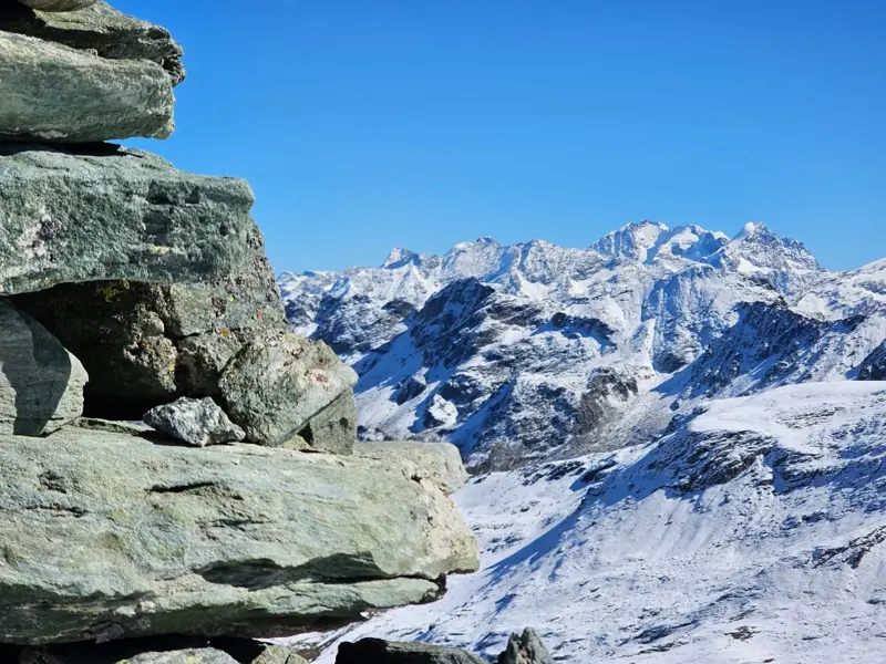 Ein Steinmann auf einem Bergpass in Graubünden mit weitem Panoramablick auf die schneebedeckten Gipfel der Alpen.