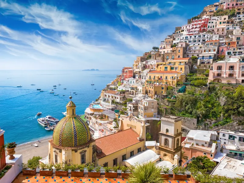 Malerischer Blick auf die bunten Häuser von Positano an der Steilküste der Amalfitana, mit einer Kirchenkuppel im Vordergrund.
