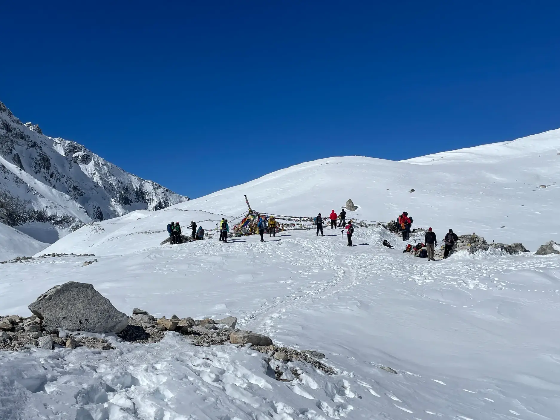 Eine Trekkinggruppe rastet an Gebetsfahnen auf dem schneebedeckten Larkya-Pass während der Manaslu-Umrundung in Nepal.