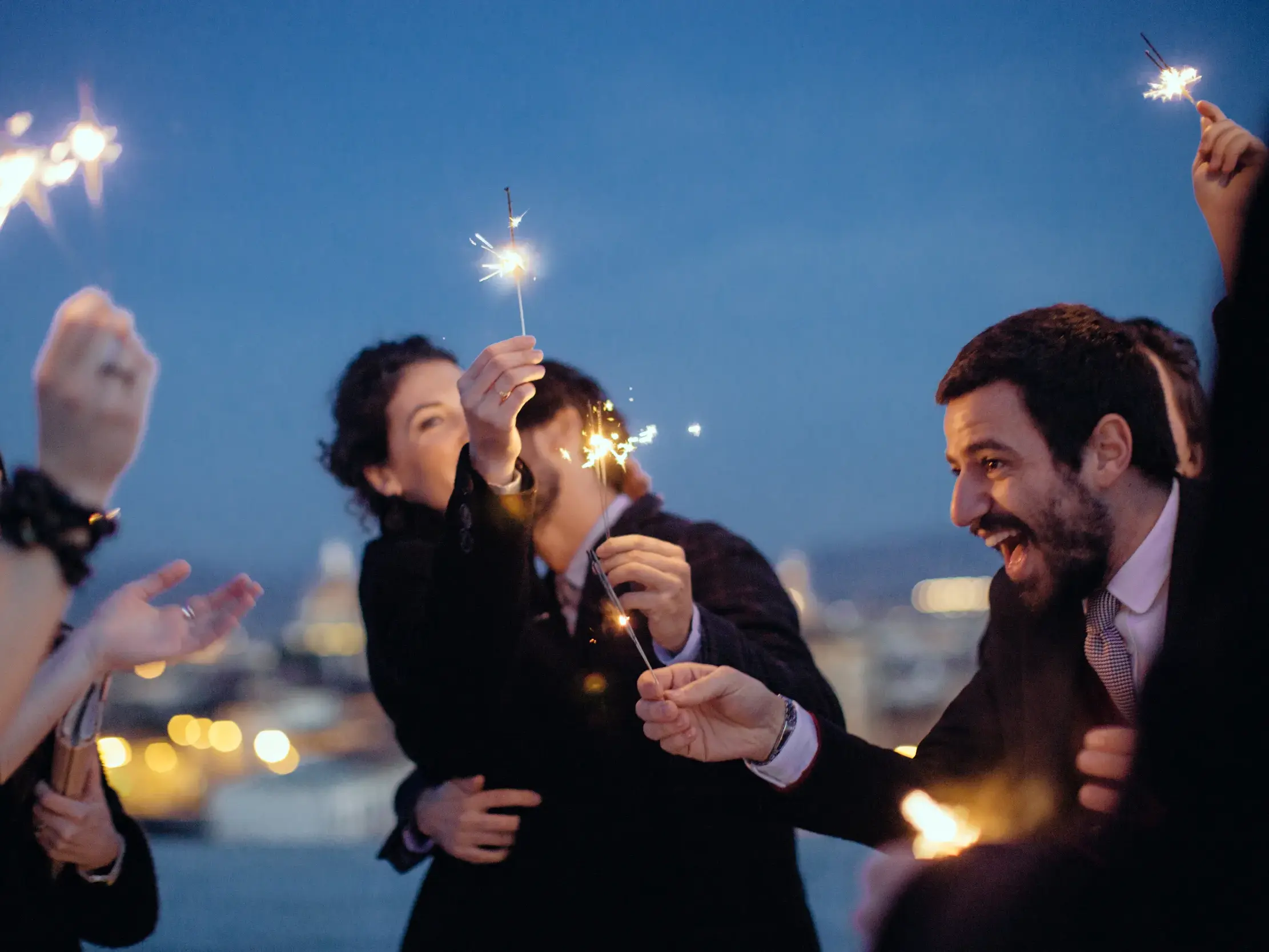 Gruppe Alleinreisender feiert ausgelassen mit Wunderkerzen Silvester über den Dächern von Valencia.