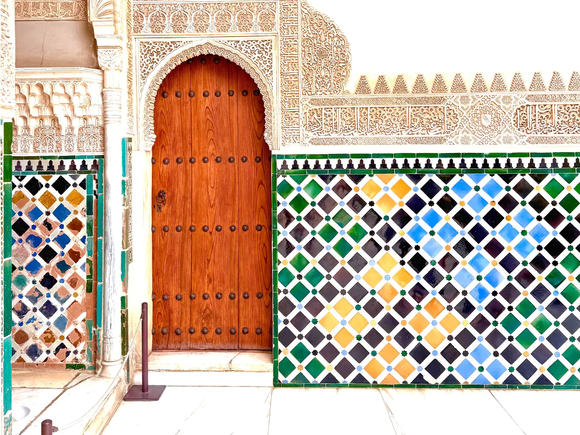 Eine kunstvolle Holztür in der Alhambra, umgeben von filigranen Stuckarbeiten und farbenfrohen Kacheln in Granada.
