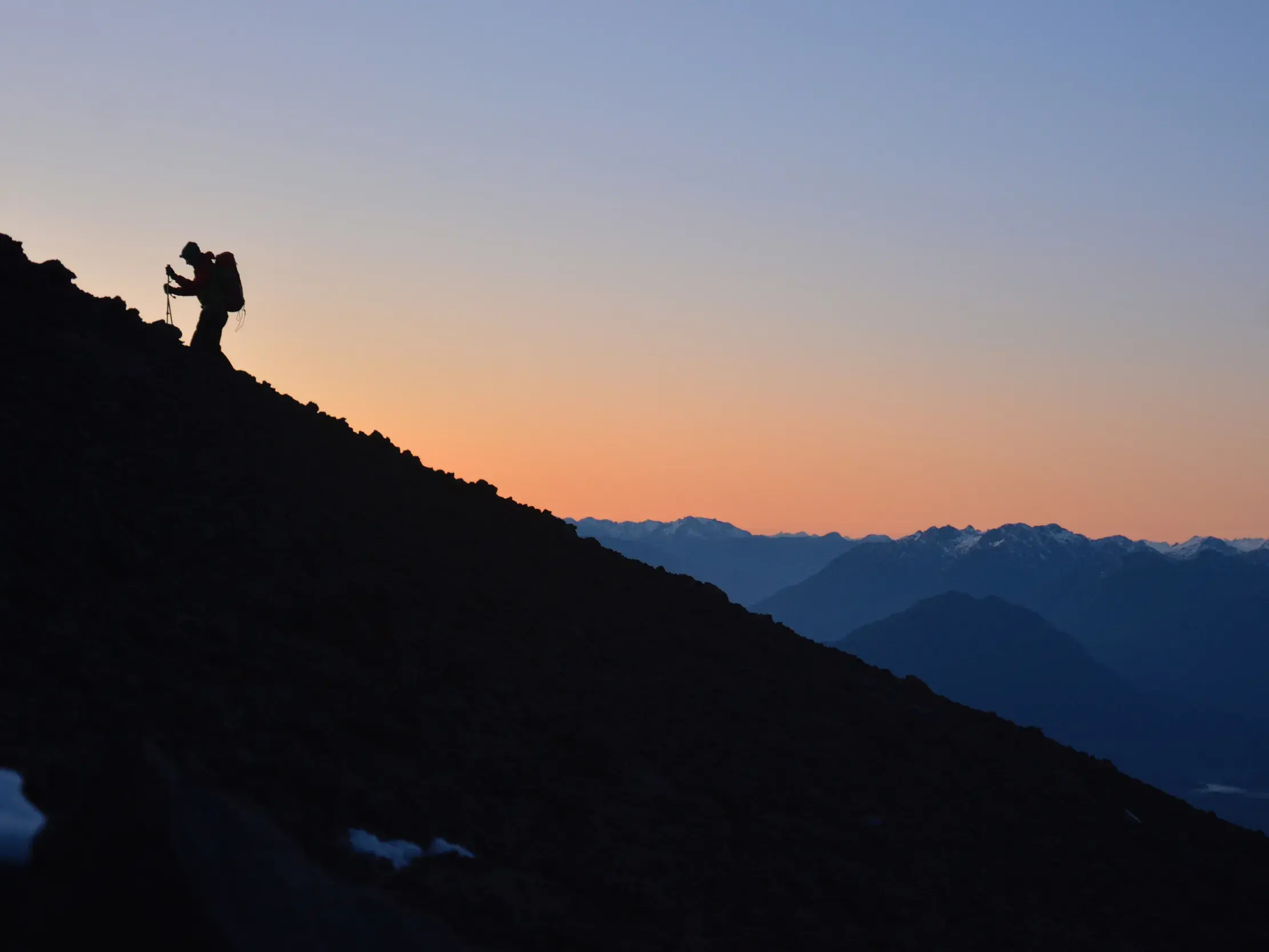 Silhouette eines Bergsteigers mit Rucksack bei der anspruchsvollen Gipfelbesteigung im Sonnenaufgang über den Bergen der Anden.