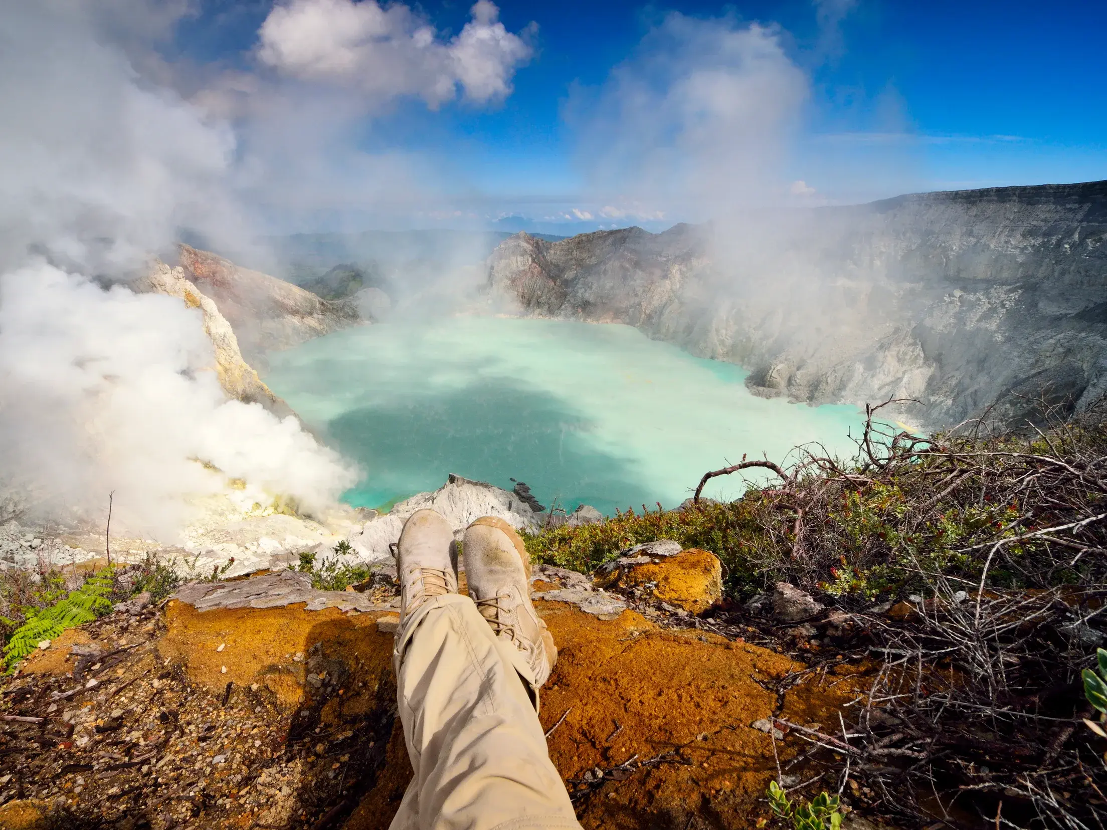 Ein Teilnehmer einer Kleingruppenreise entspannt am Rand  eines Kraters mit Blick auf den dampfenden türkisen See.