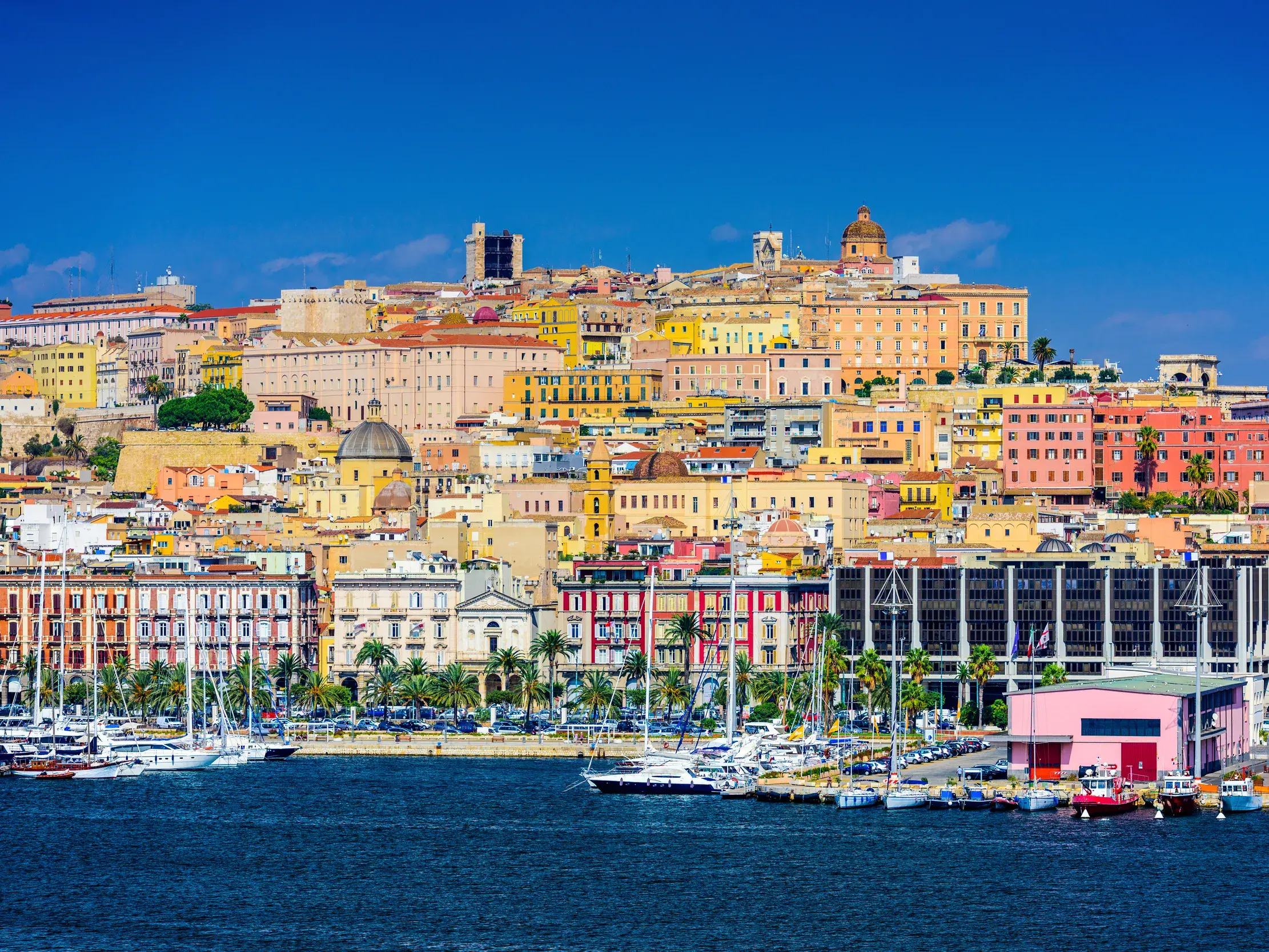 Panoramablick auf die historische Altstadt von Cagliari auf Sardinien mit ihrem Hafen voller Yachten unter blauem Himmel.