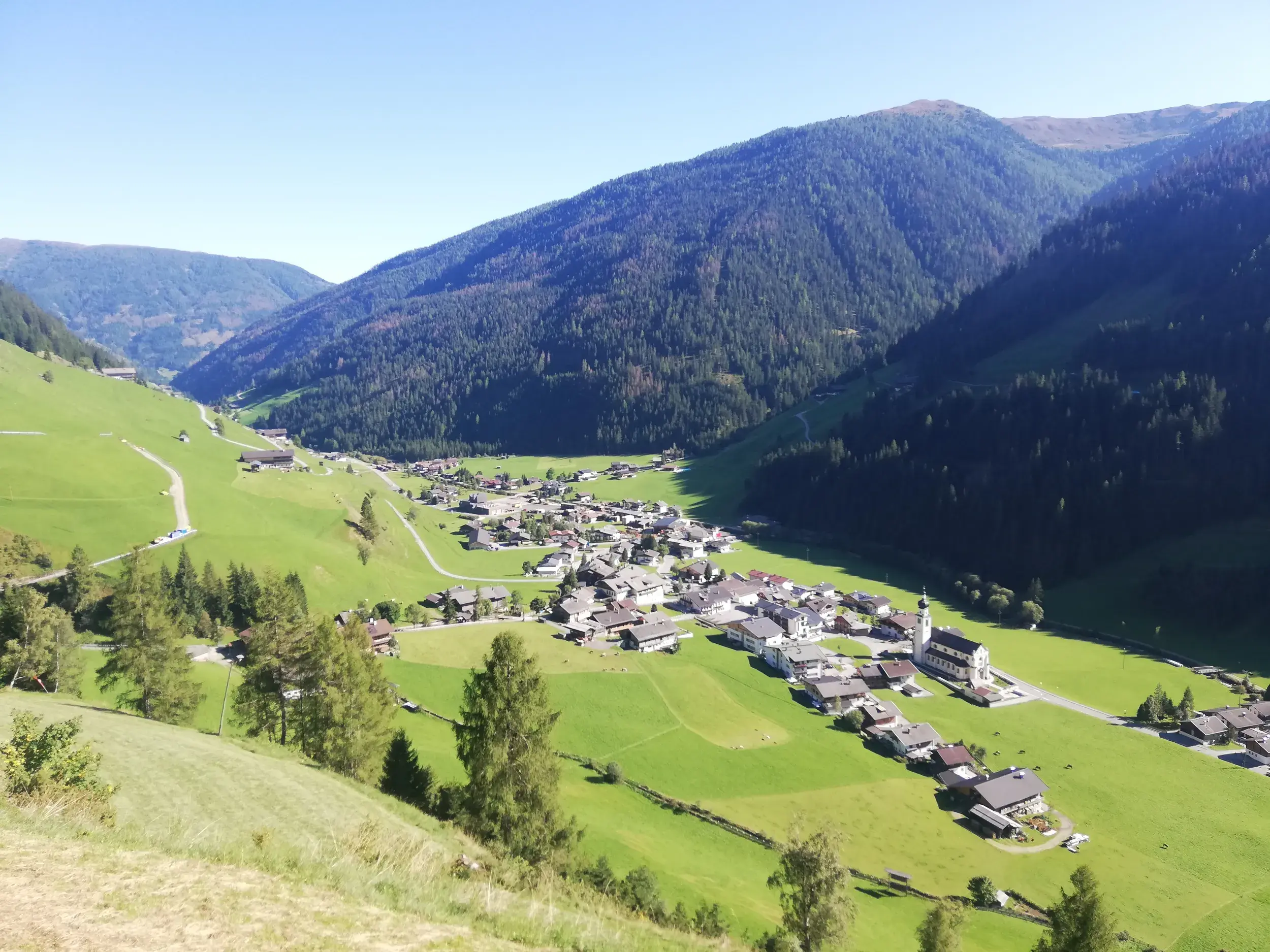Sonnige Aussicht von einem Berghang auf das Dorf Innervillgraten, das idyllisch im grünen Villgratental in Osttirol liegt.