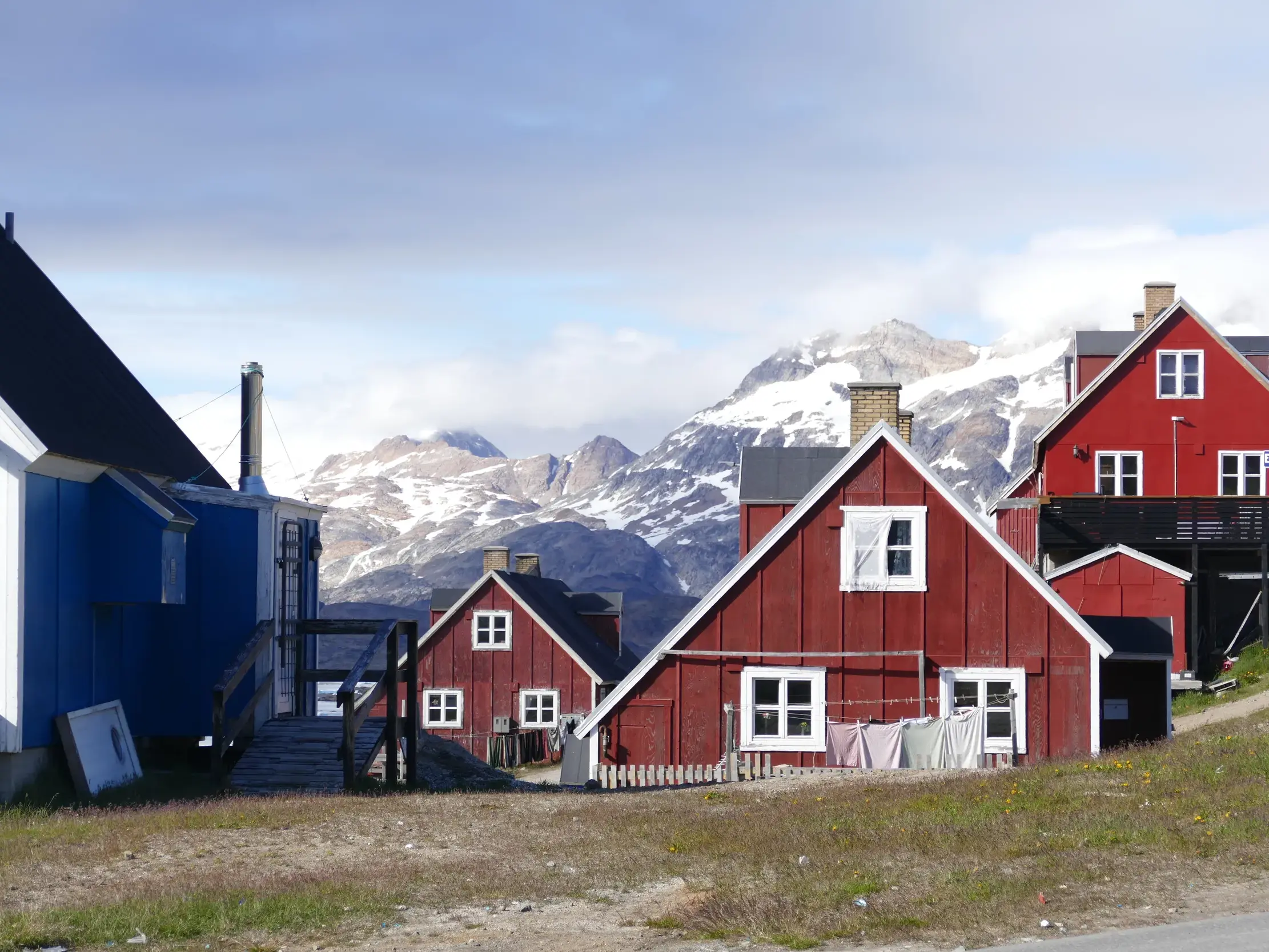 Bunte Holzhäuser der Siedlung Tasiilaq in Ostgrönland mit Blick auf die beeindruckende, schneebedeckte Berglandschaft.