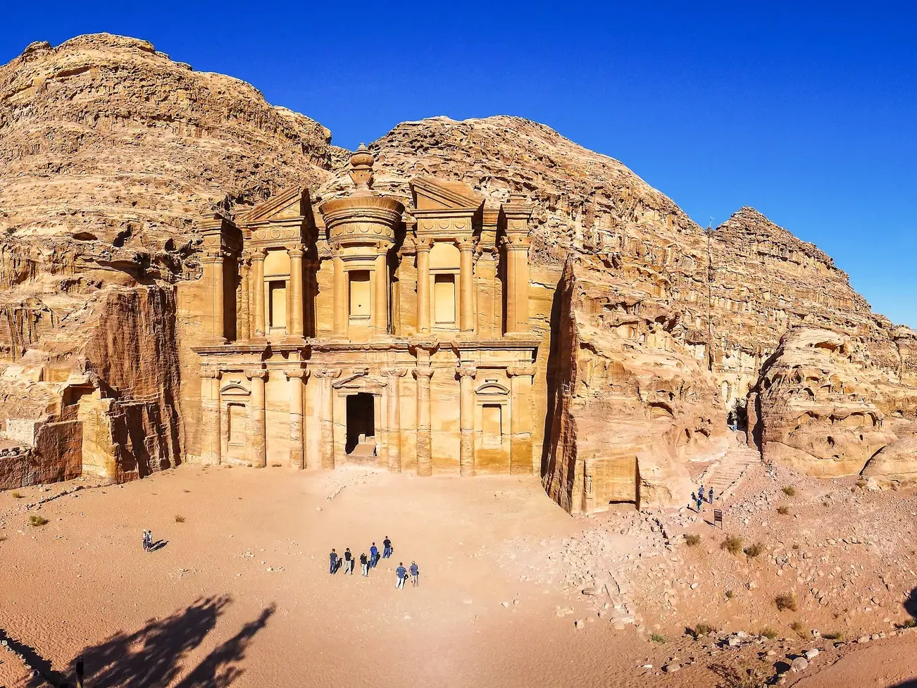 Eine Reisegruppe bestaunt das monumentale, in Fels gehauene Kloster Ad-Deir in der antiken Stadt Petra in Jordanien.