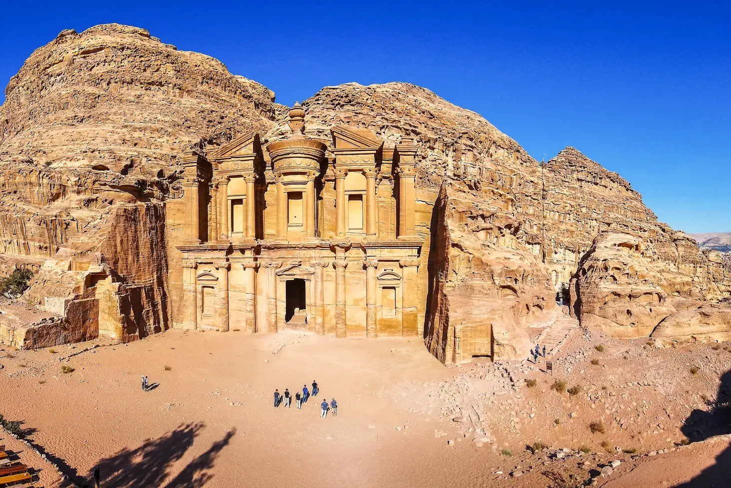 Eine kleine Wandergruppe steht vor dem monumentalen Felsenkloster Ed-Deir in Petra, einem Highlight der Jordanien-Reise.