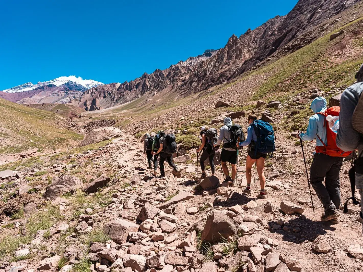 Trekking-Gruppe auf steinigem Pfad im Aconcagua-Provinzpark mit Blick auf einen schneebedeckten Gipfel der Anden.