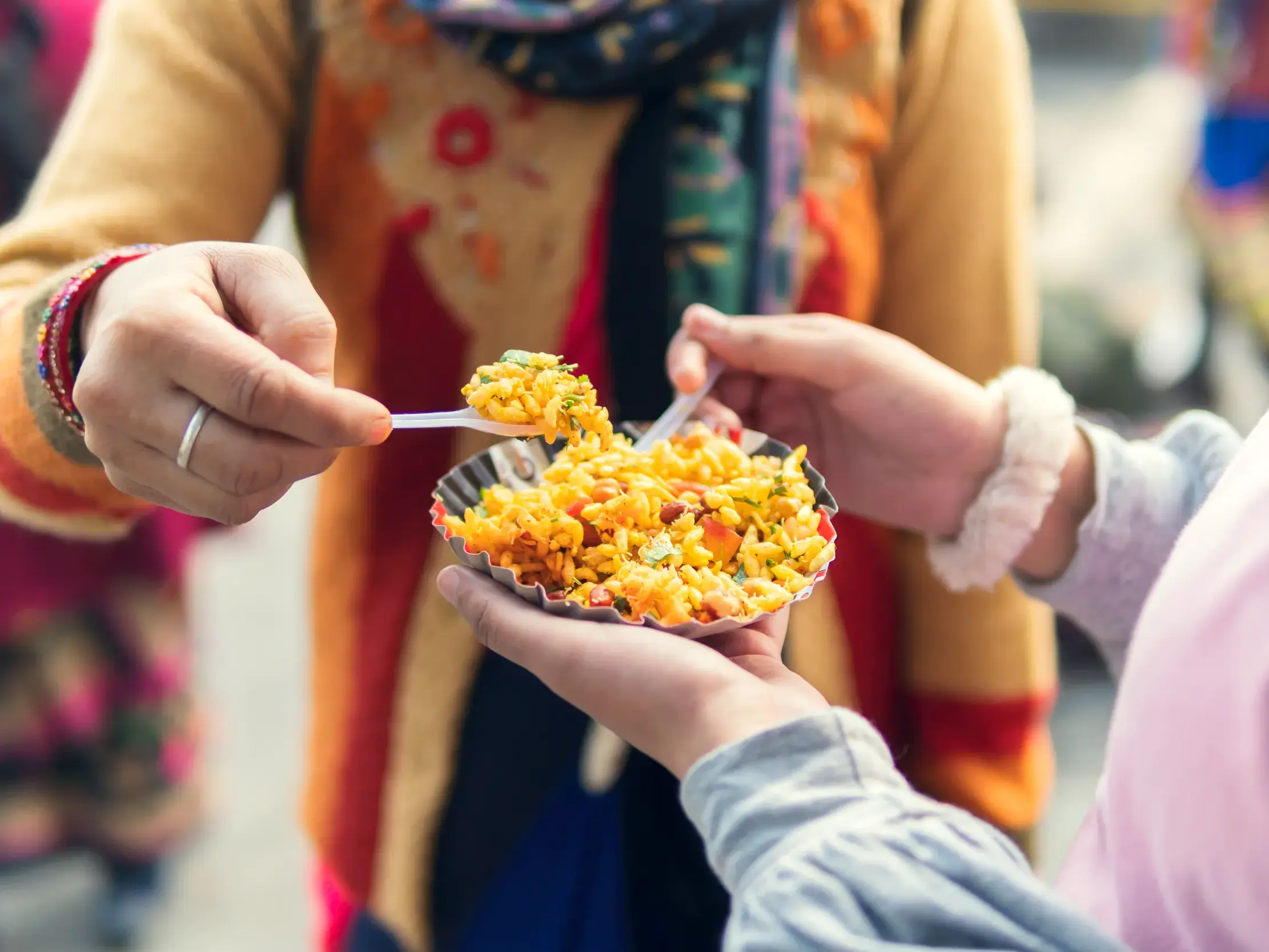 Zwei junge Leute teilen sich auf einer Gruppenreise in Indien eine Schale mit würzigem Puffreis, ein typisches Streetfood.