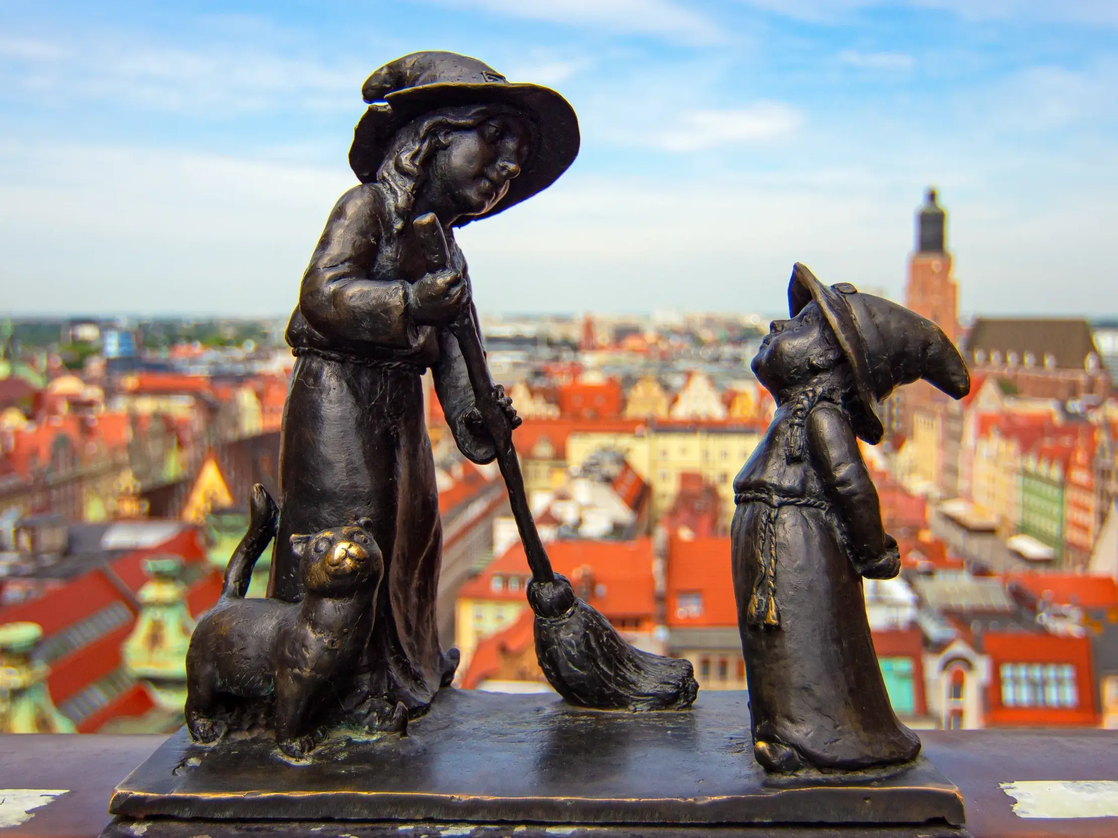Zwei der berühmten Breslauer Zwerge als Bronzestatuen auf einem Sims mit weitem Blick über die Dächer der Altstadt von Breslau.