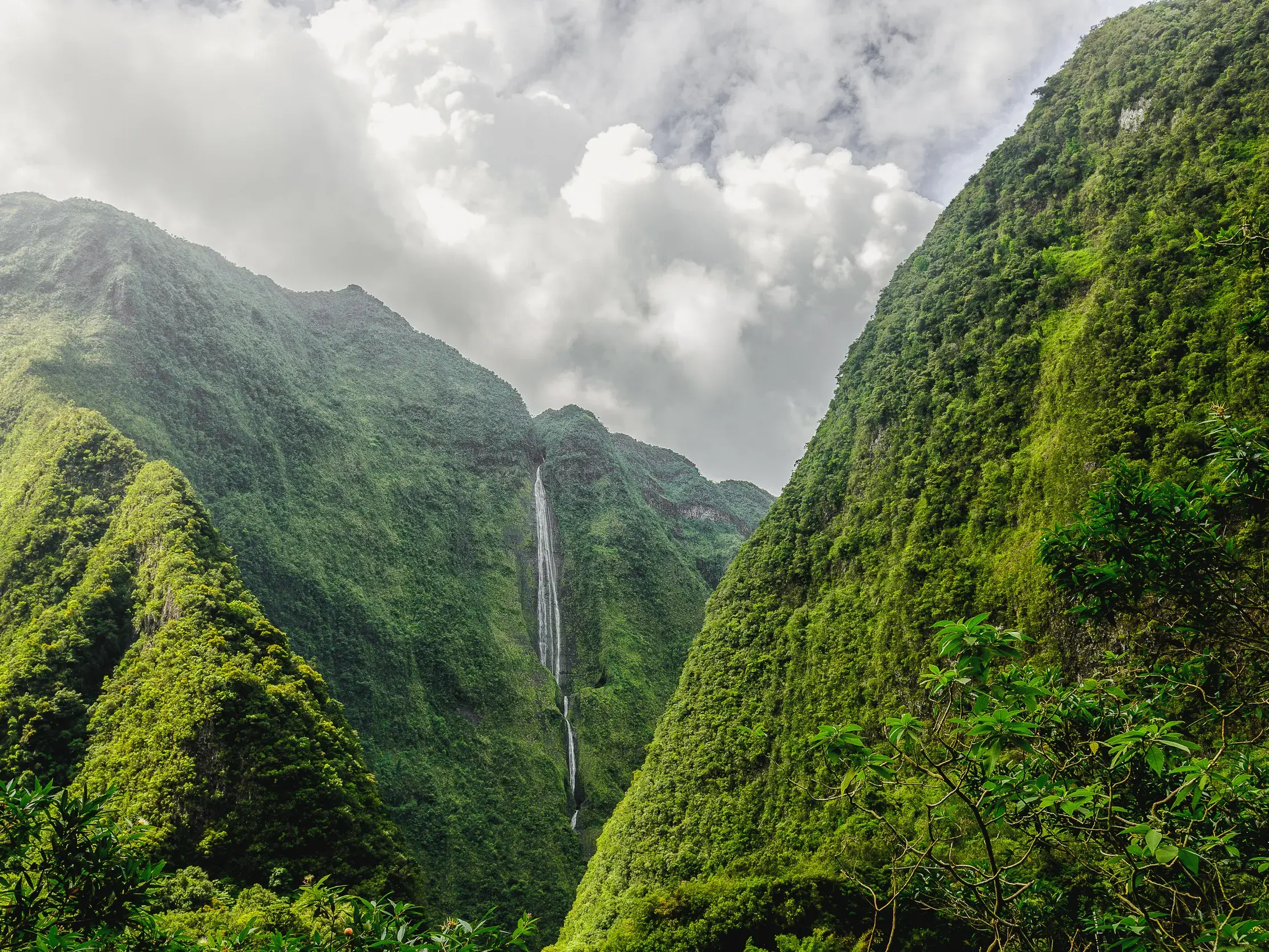 Spektakulärer Ausblick beim Wandern auf die üppig grünen Berge und einen Wasserfall im Cirque de Salazie auf La Réunion.