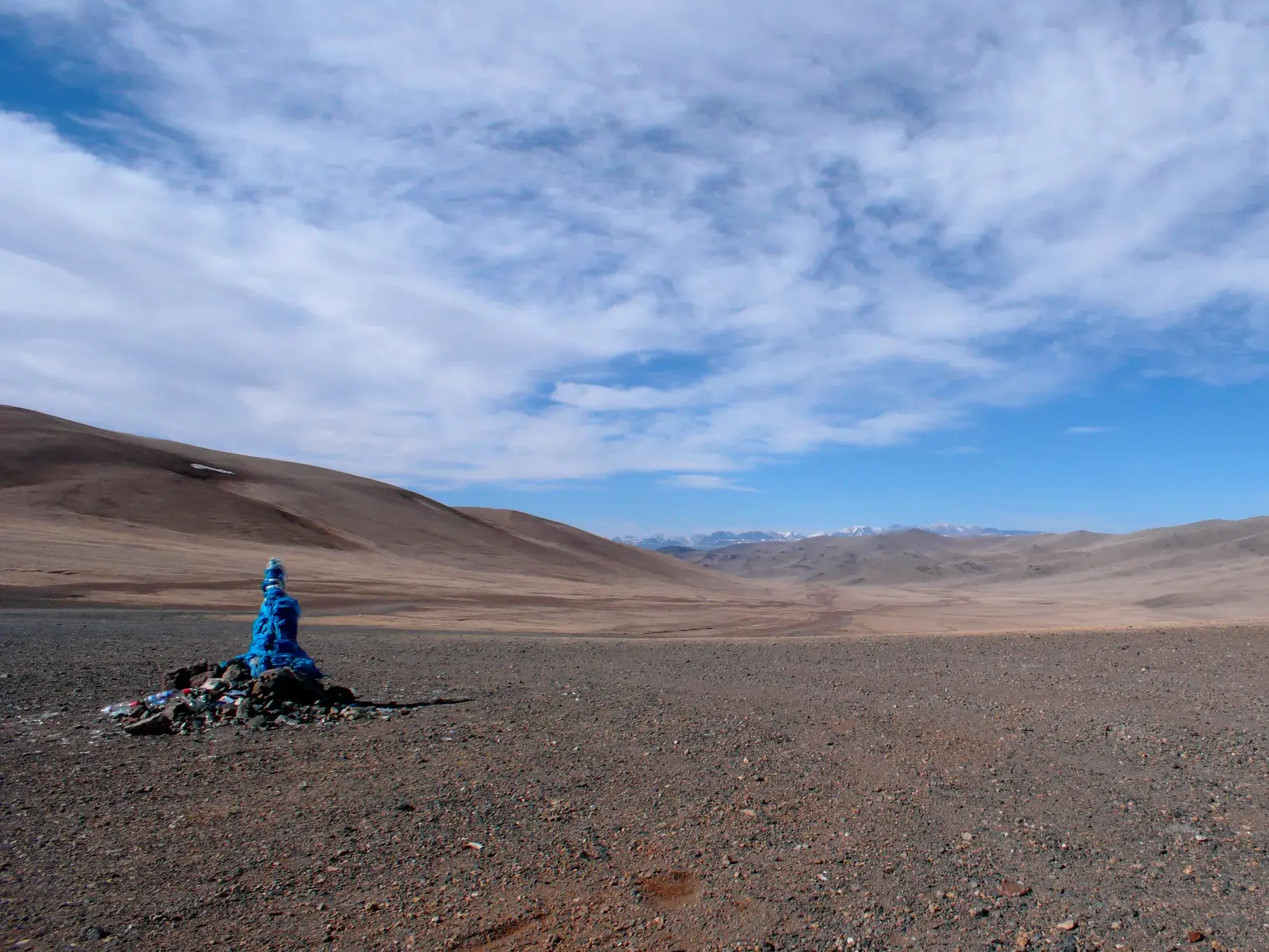 Traditioneller Ovoo-Steinhaufen mit blauen Tüchern in der weiten Steppe des mongolischen Altai-Gebirges unter Wolkenhimmel.