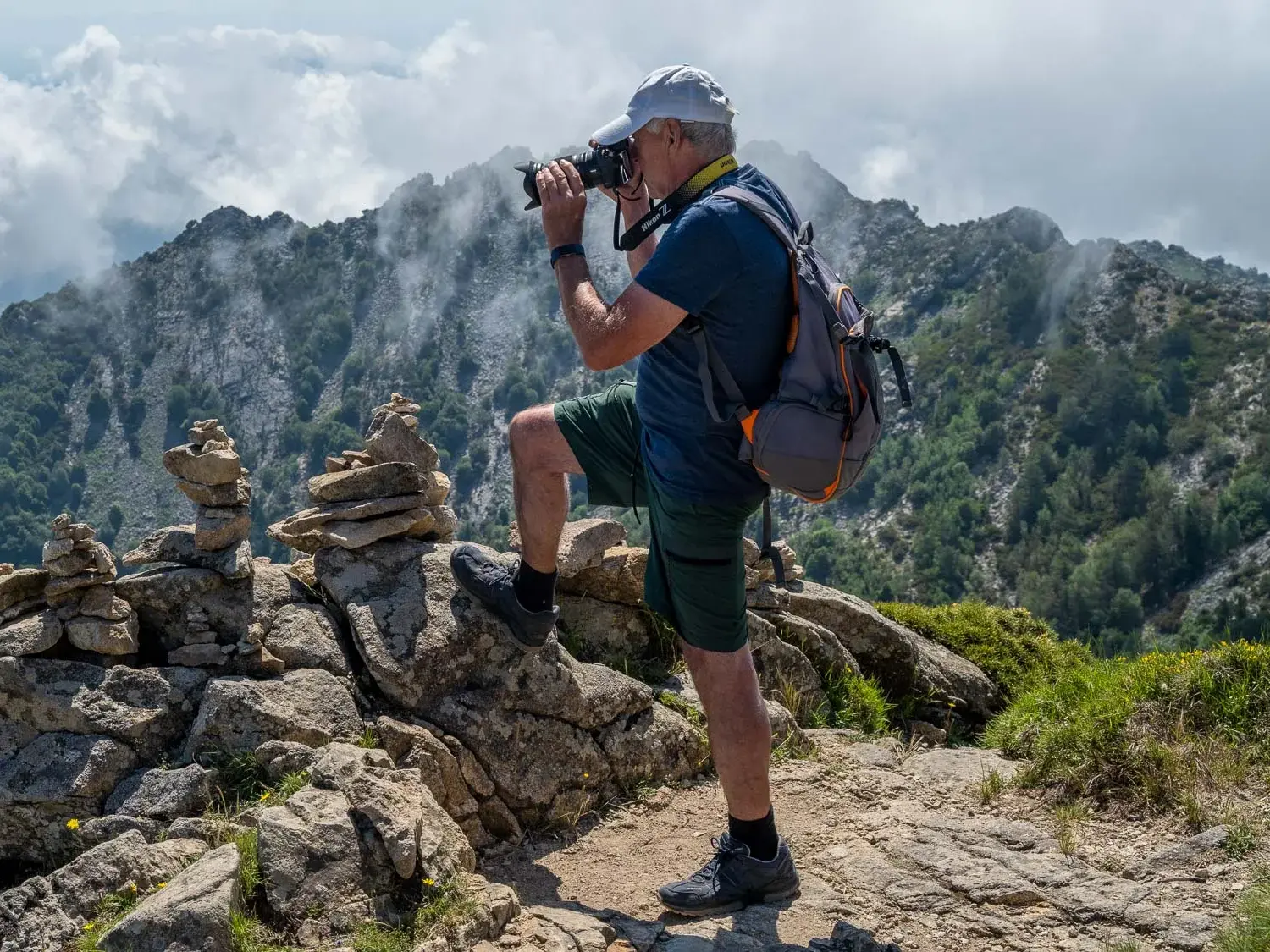 Ein Wanderer fotografiert auf dem GTE-Trekkingpfad auf Elba von einem Gipfel mit Steinmännchen die Bergkulisse.