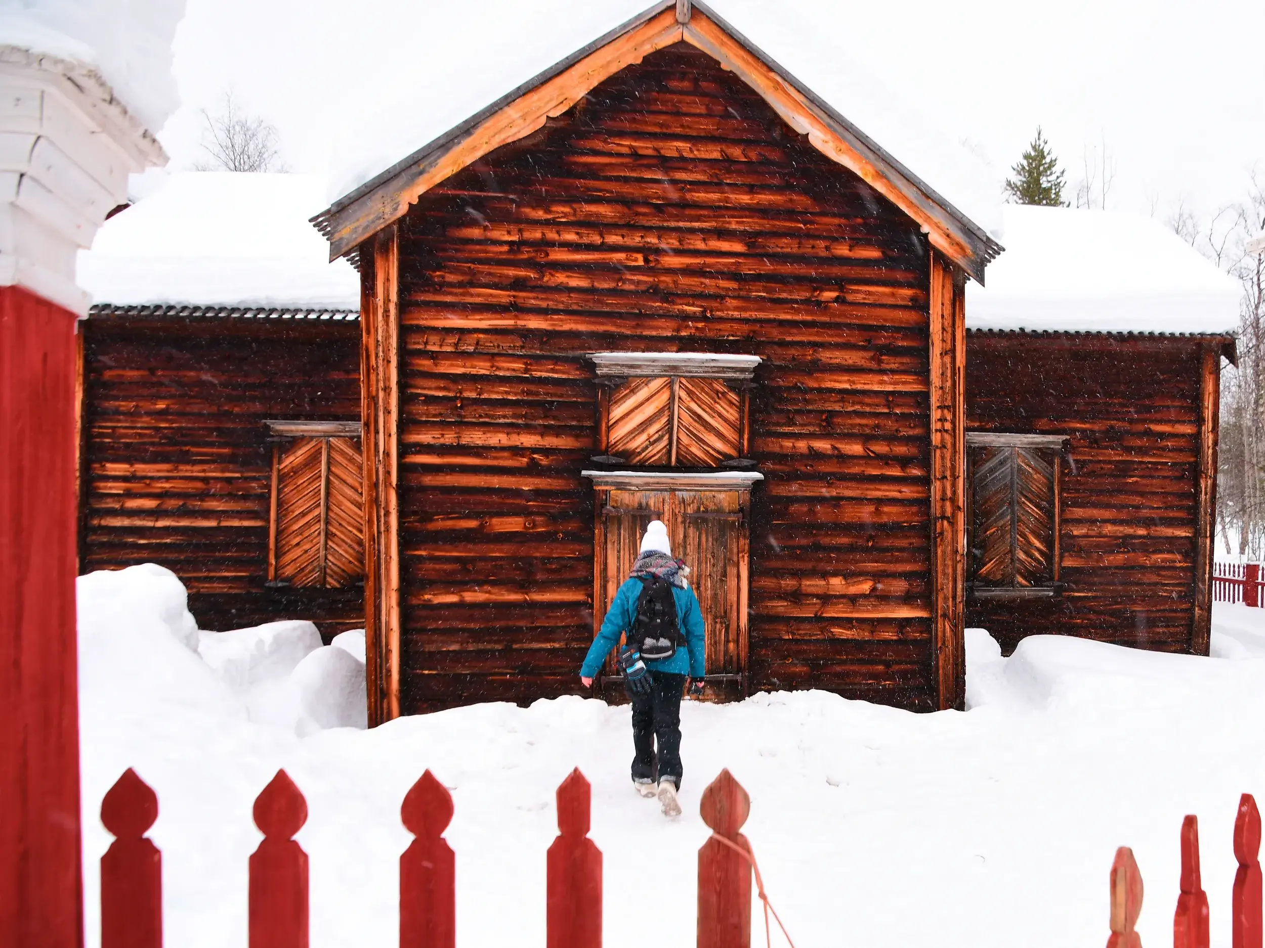 Eine Teilnehmerin einer Studiosus-Studienreise geht durch hohen Schnee zur historischen Holzkirche Pielpajärvi in Finnland.