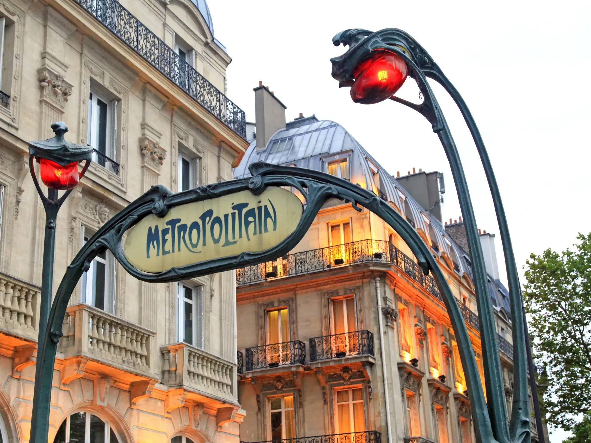 Ikonischer Metropolitain-Eingang im Jugendstil mit rot leuchtenden Lampen vor einer eleganten Hausfassade in Paris.