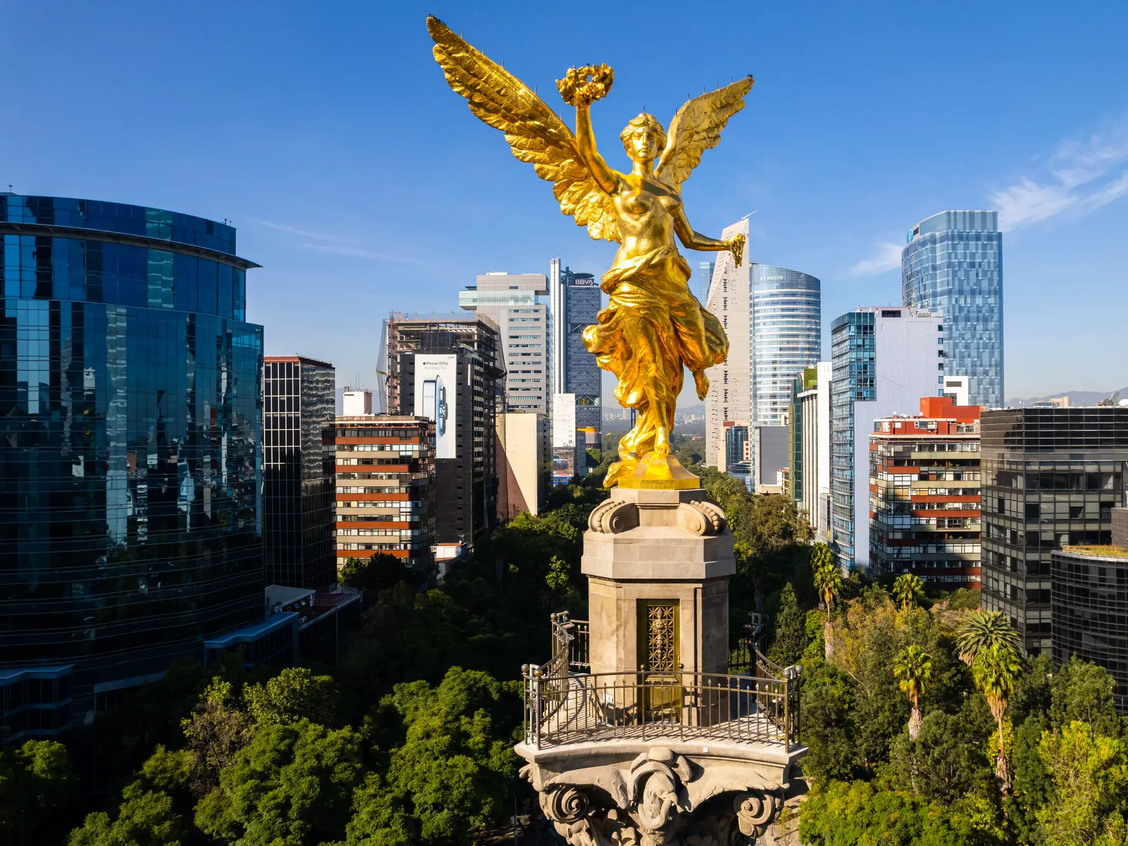 Der goldene Unabhängigkeitsengel über grünen Baumwipfeln vor der beeindruckenden Skyline der Megacity Mexiko-Stadt.
