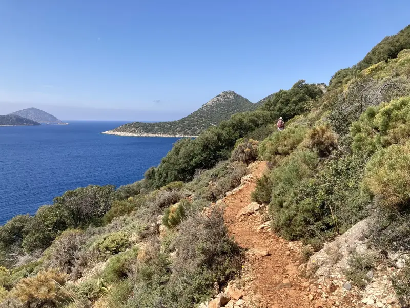 Eine Wanderin auf einem schmalen Pfad des Lykischen Wegs mit Panoramablick über die türkische Mittelmeerküste.
