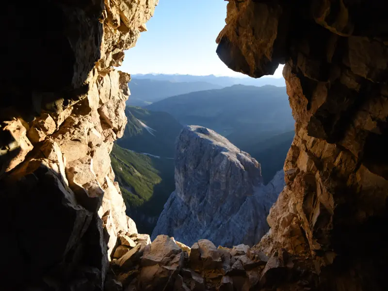 Blick aus einem alten Kriegsstollen am Lagazuoi auf die weite Berglandschaft der Dolomiten bei Sonnenaufgang.