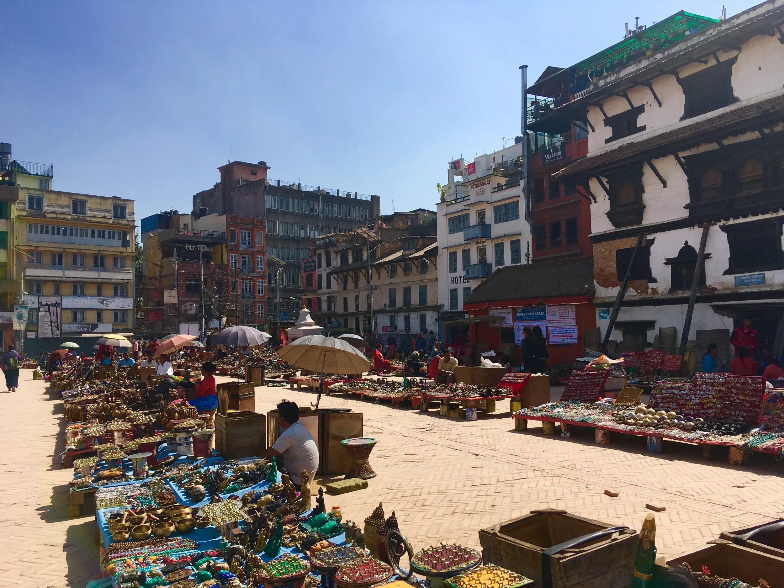 Zahlreiche Marktstände mit nepalesischem Kunsthandwerk auf einem belebten Platz in der Altstadt von Kathmandu bei Sonnenschein.