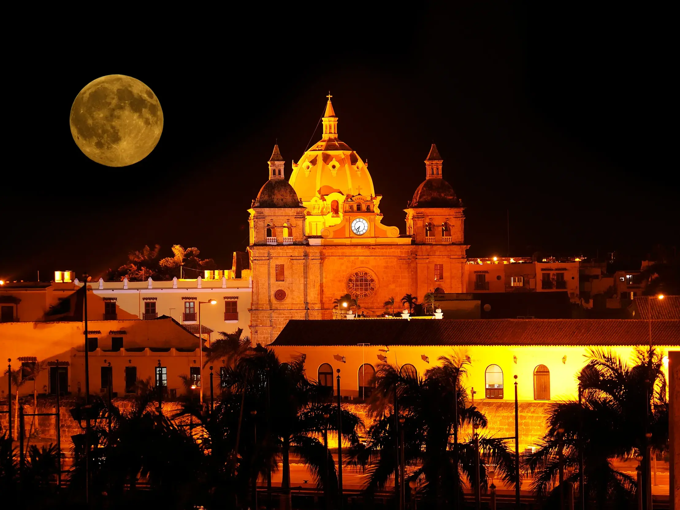Die gold beleuchtete Kirche San Pedro Claver in der Altstadt von Cartagena bei Nacht mit einem großen Vollmond am Himmel.