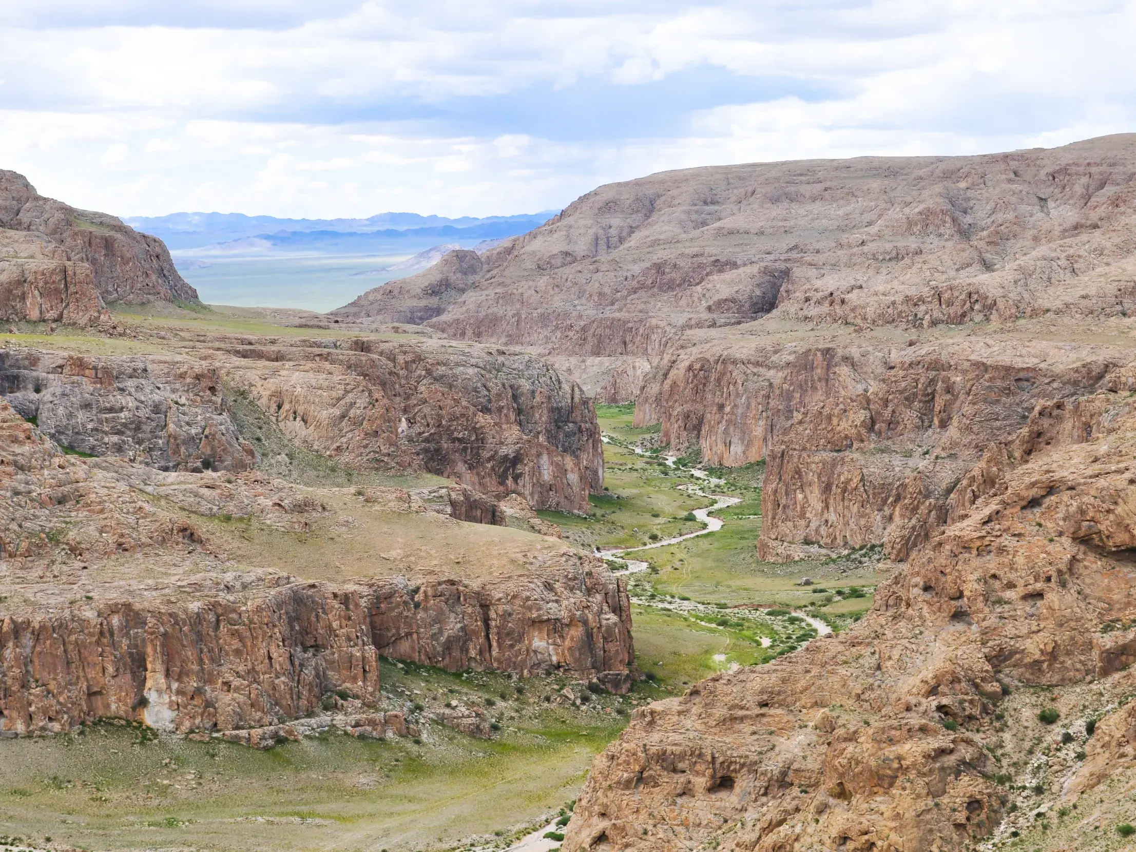 Majestätischer Ausblick beim Wandern am Ikh Khairkhan Bergmassiv in ein felsiges Tal mit Blick auf die weite Steppe der Mongolei.