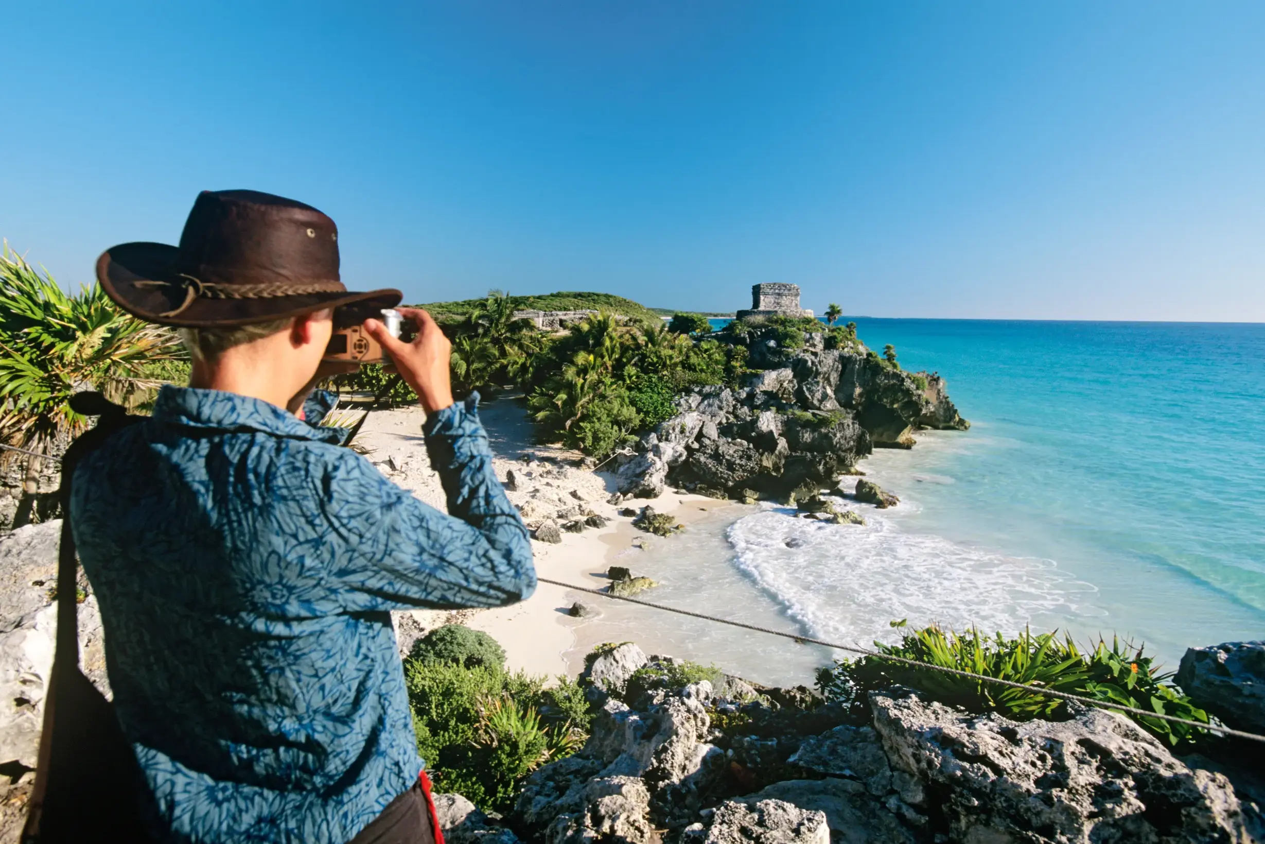 Junger Reisender mit Hut fotografiert die berühmte Maya-Ruine von Tulum über dem türkisblauen Karibischen Meer.