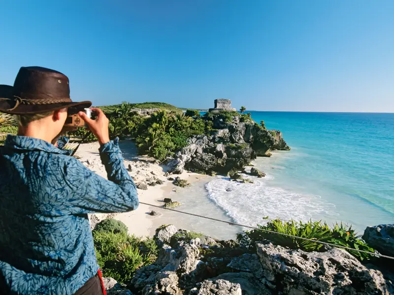 Junger Reisender mit Hut fotografiert die berühmte Maya-Ruine von Tulum über dem türkisblauen Karibischen Meer.