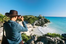 Junger Reisender mit Hut fotografiert die berühmte Maya-Ruine von Tulum über dem türkisblauen Karibischen Meer.