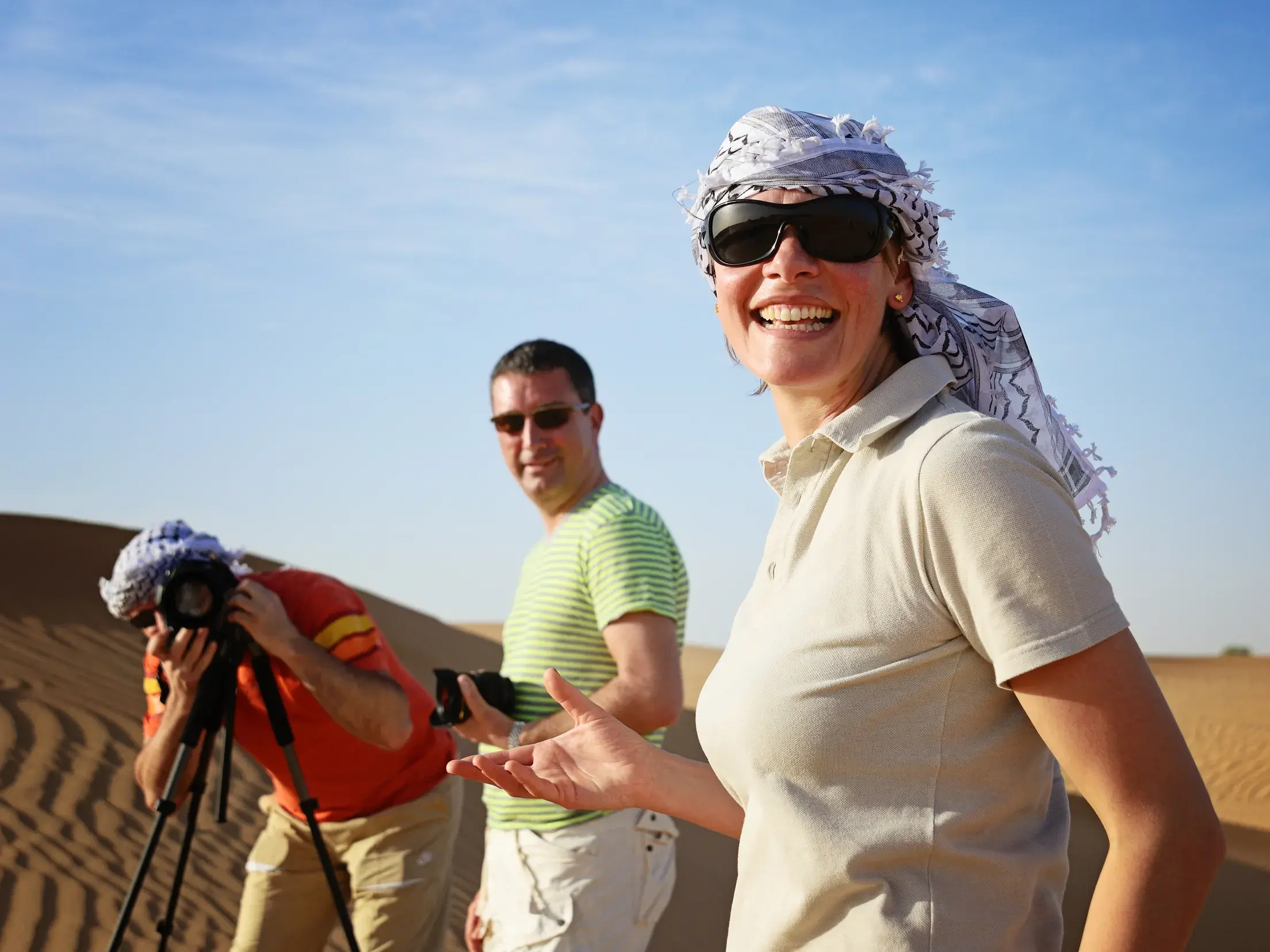 Lachende Frau mit Kopftuch auf einer Reise in kleiner Gruppe in der Wüste Wadi Ram in Jordanien, während Reisende fotografieren.