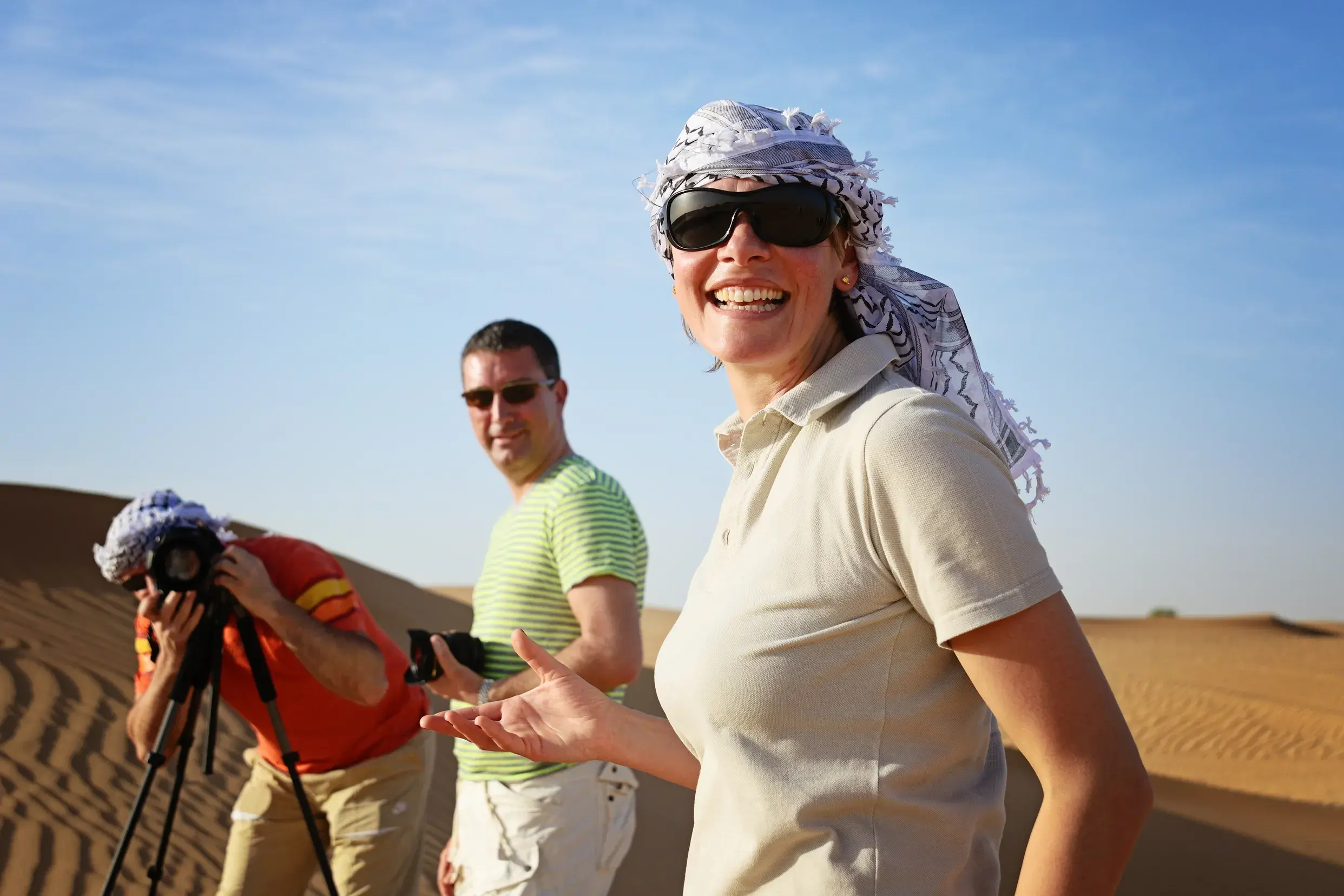 Lachende Frau mit Kopftuch auf einer Reise in kleiner Gruppe in der Wüste Wadi Ram in Jordanien, während Reisende fotografieren.