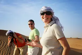 Lachende Frau mit Kopftuch auf einer Reise in kleiner Gruppe in der Wüste Wadi Ram in Jordanien, während Reisende fotografieren.
