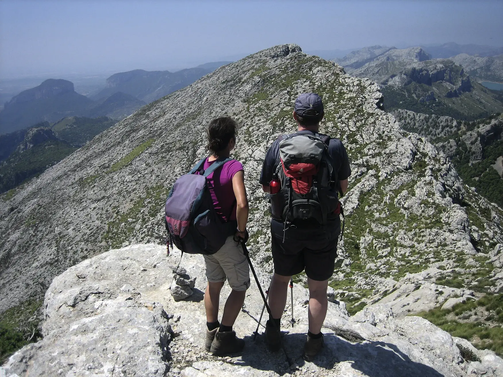 Zwei Wanderer mit Rucksäcken auf dem Gipfel des Puig de Massanella blicken über die Serra de Tramuntana auf Mallorca.
