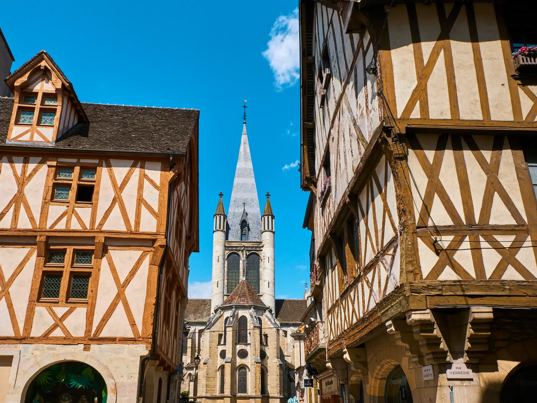 Historische Fachwerkhäuser in Dijon, die an einem sonnigen Tag den Blick auf den Kirchturm der Kirche Notre-Dame freigeben.