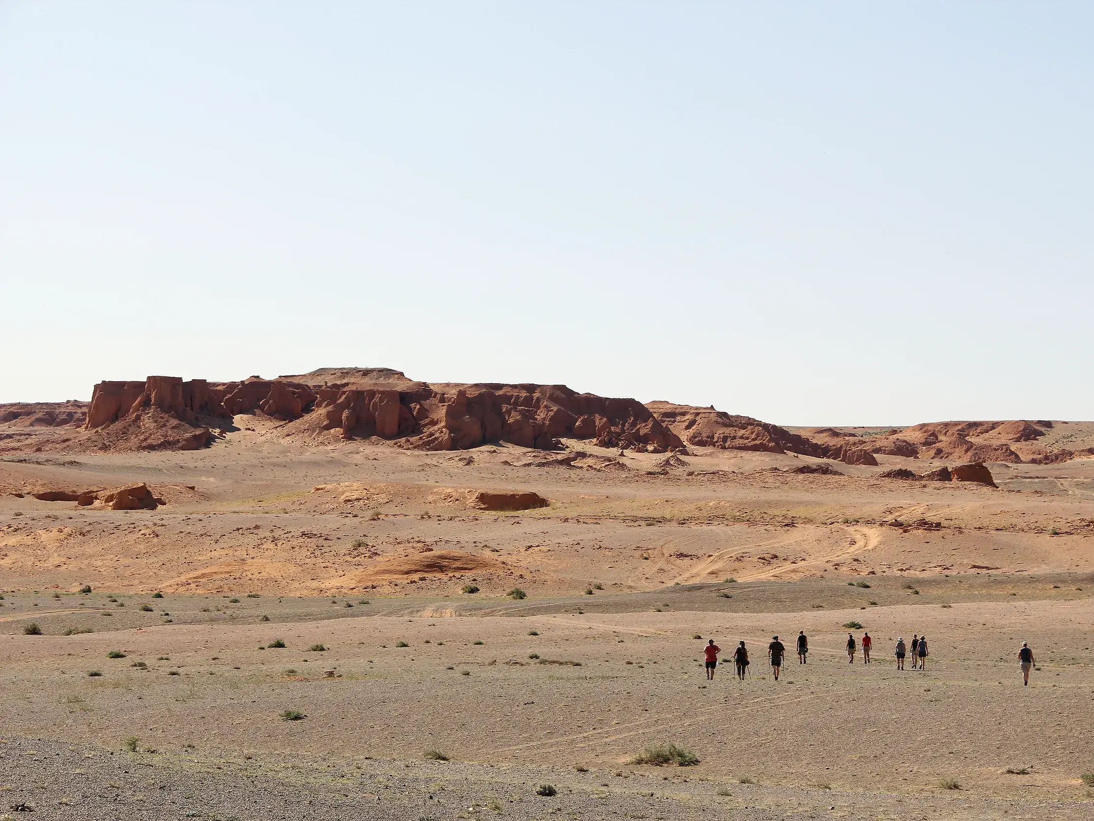 Eine Wandergruppe durchquert die weite Landschaft der Wüste Gobi auf dem Weg zu den rot leuchtenden Klippen von Bayanzag.