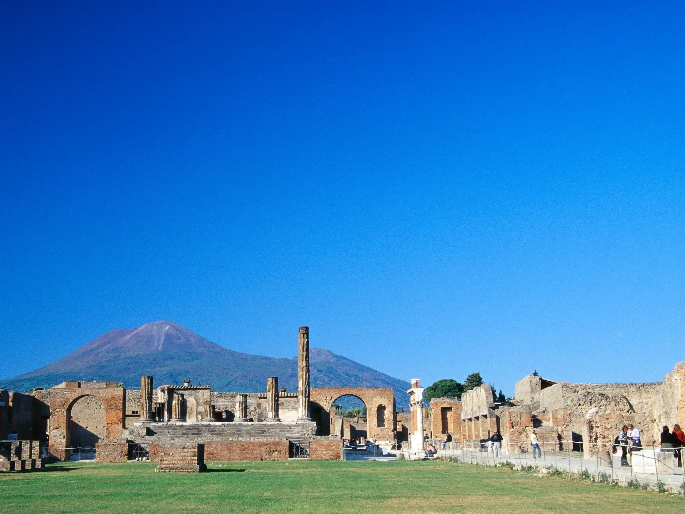 Reisende erkunden die antiken Ruinen von Pompeji mit Blick auf den Vulkan Vesuv am Golf von Neapel an einem sonnigen Tag.