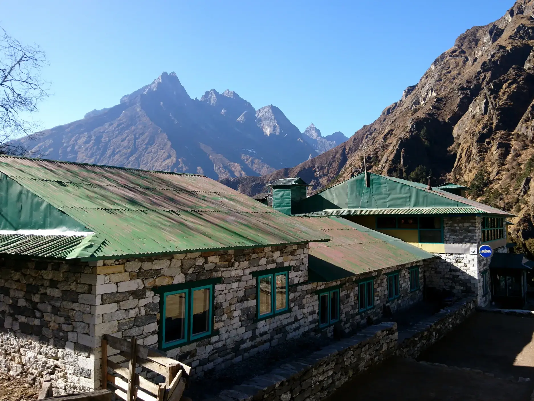 Eine typische Trekking-Lodge aus Stein in einem Sherpa-Dorf im Khumbu-Tal vor den hohen, felsigen Gipfeln des Himalaya.