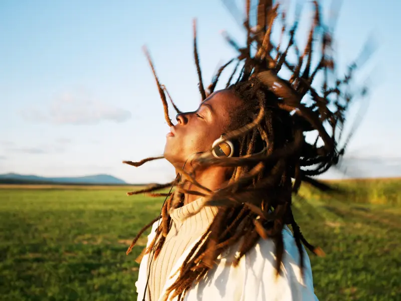 Eine Person wirft ihre Dreadlocks schwungvoll zurück und genießt die Sonne auf einem weiten, grünen Feld in den USA.