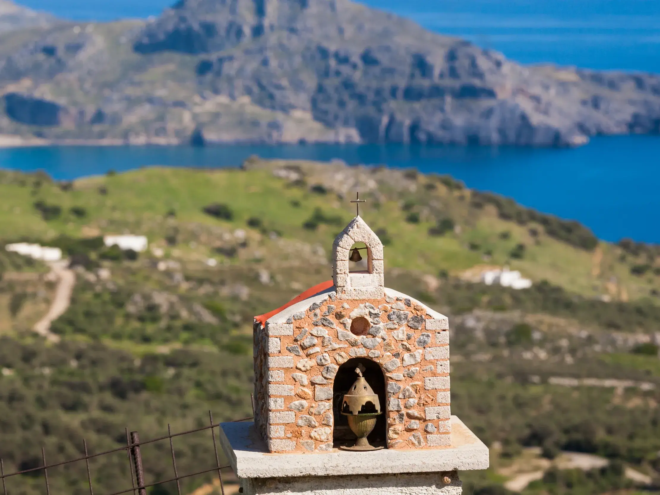 Traditioneller Steinschrein mit Glocke an einem Wanderweg mit Blick auf die felsige Südküste und das Meer auf Kreta.