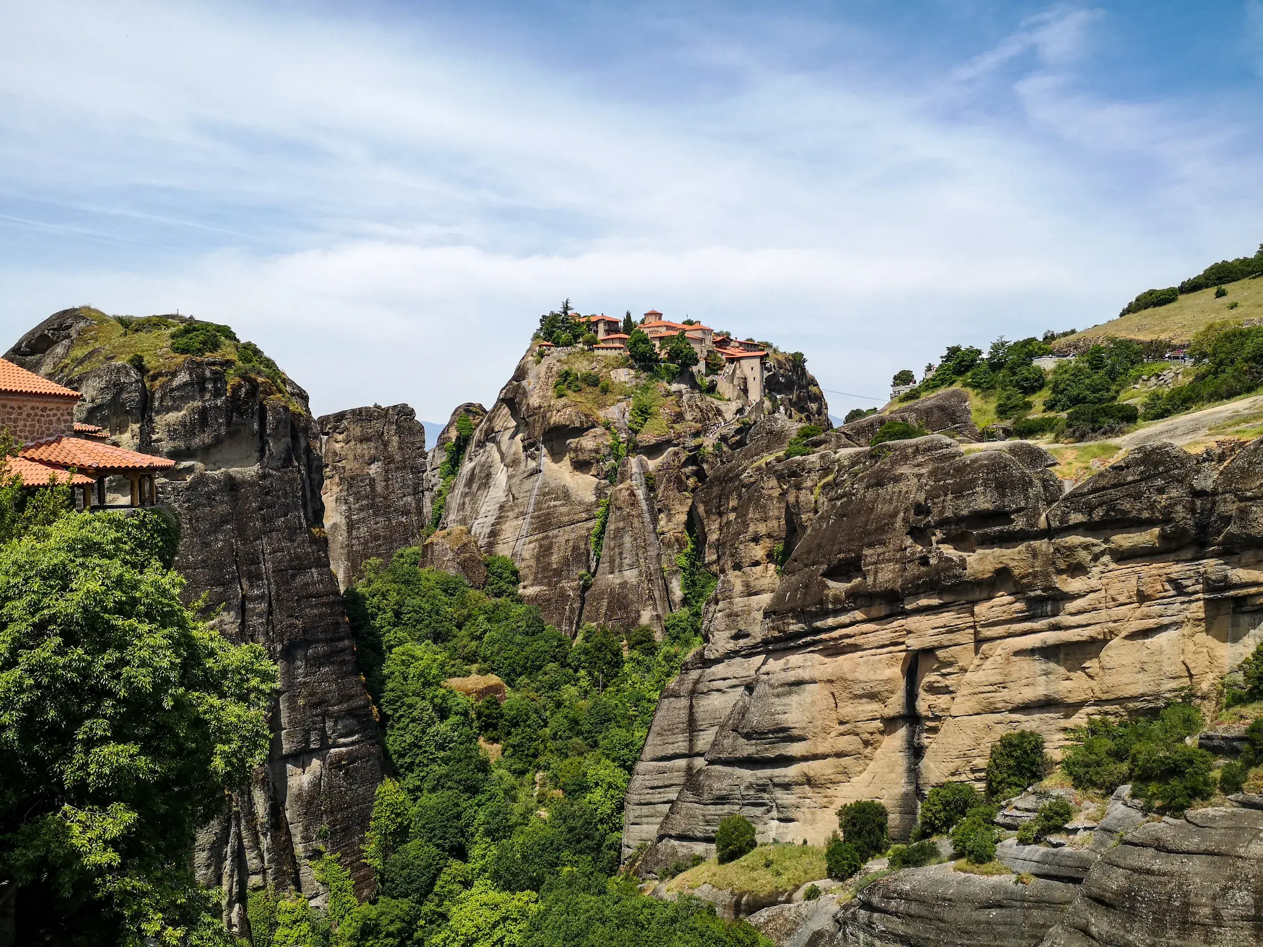 Ein Meteora Kloster thront auf einem spektakulären Felsturm, gesehen von einem Wanderweg in der Felslandschaft Griechenlands.