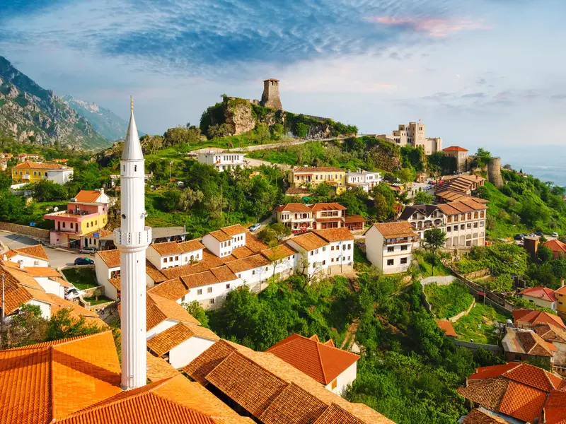 Panoramablick über die Dächer der Altstadt von Kruja mit der Burg von Skanderbeg und einem Minarett im Vordergrund.