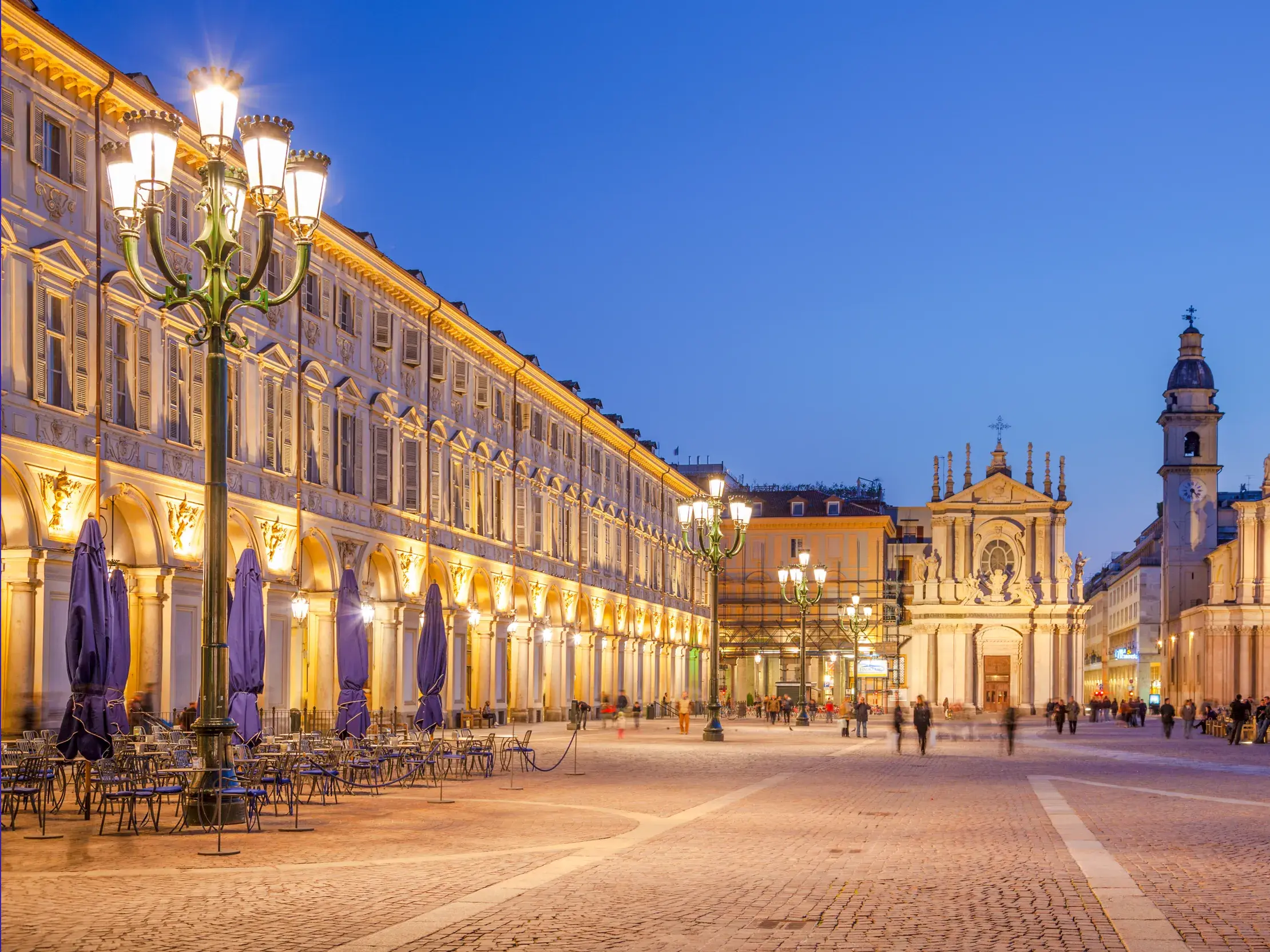 Die elegante Piazza San Carlo in Turin zur blauen Stunde mit beleuchteten Arkaden und barocken Zwillingskirchen im Hintergrund.