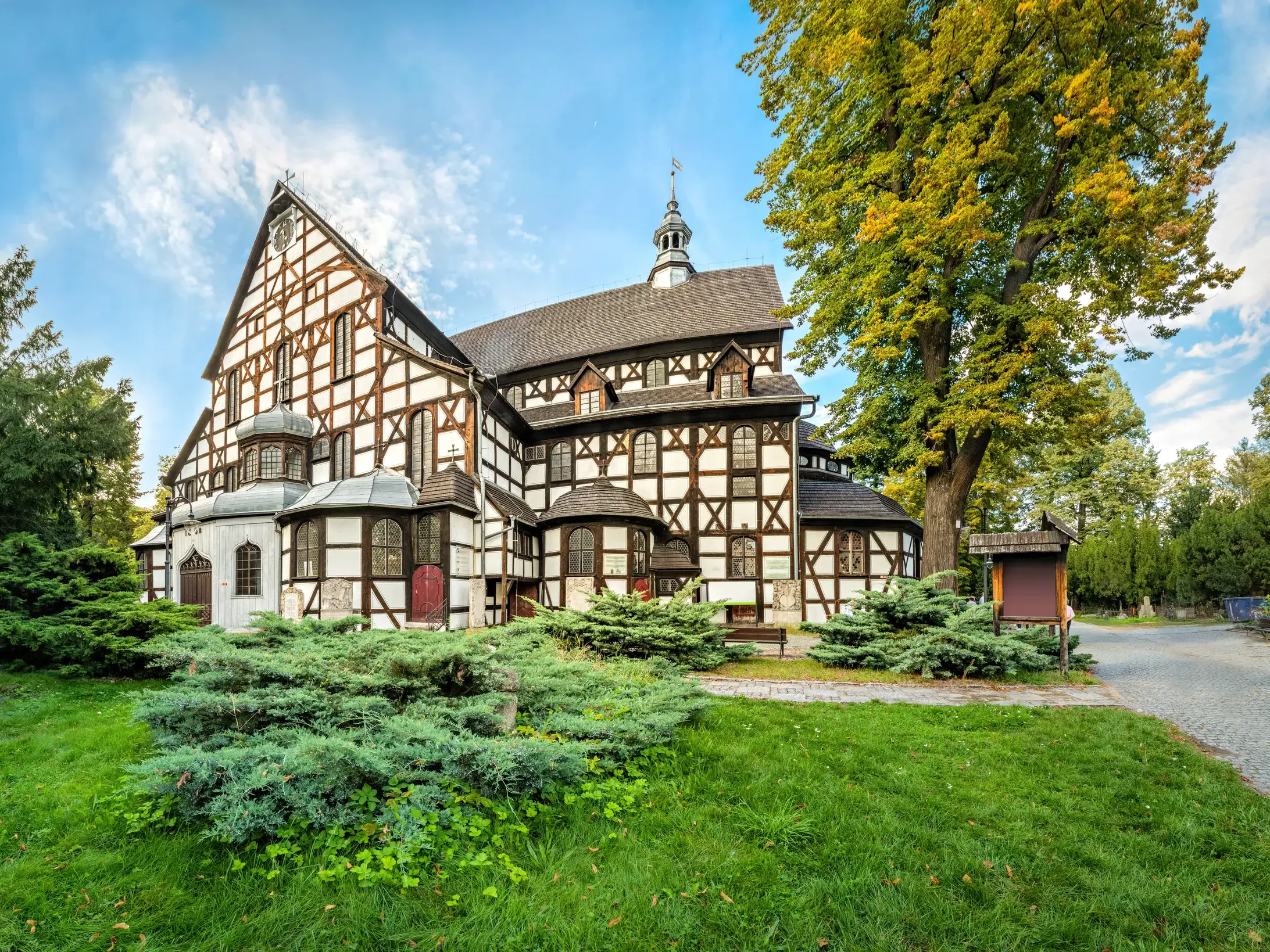 Die imposante Friedenskirche in Swidnica (UNESCO-Welterbe) als eindrucksvoller Fachwerkbau, umgeben von Bäumen und Wiesen.