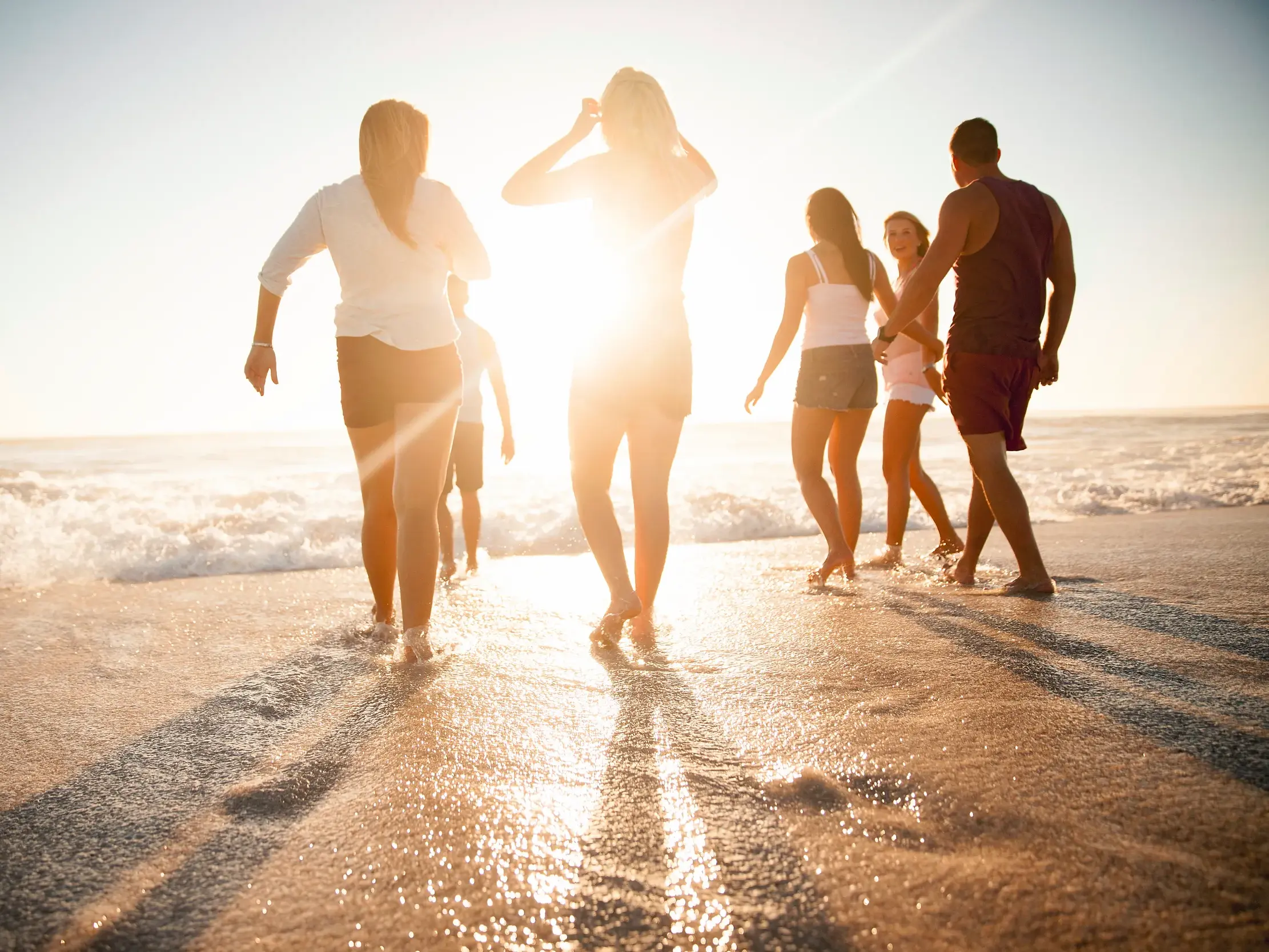 Junge Reisende einer Kleingruppenreise spazieren bei Sonnenuntergang durch das seichte Wasser an einem Karibikstrand auf Kuba.