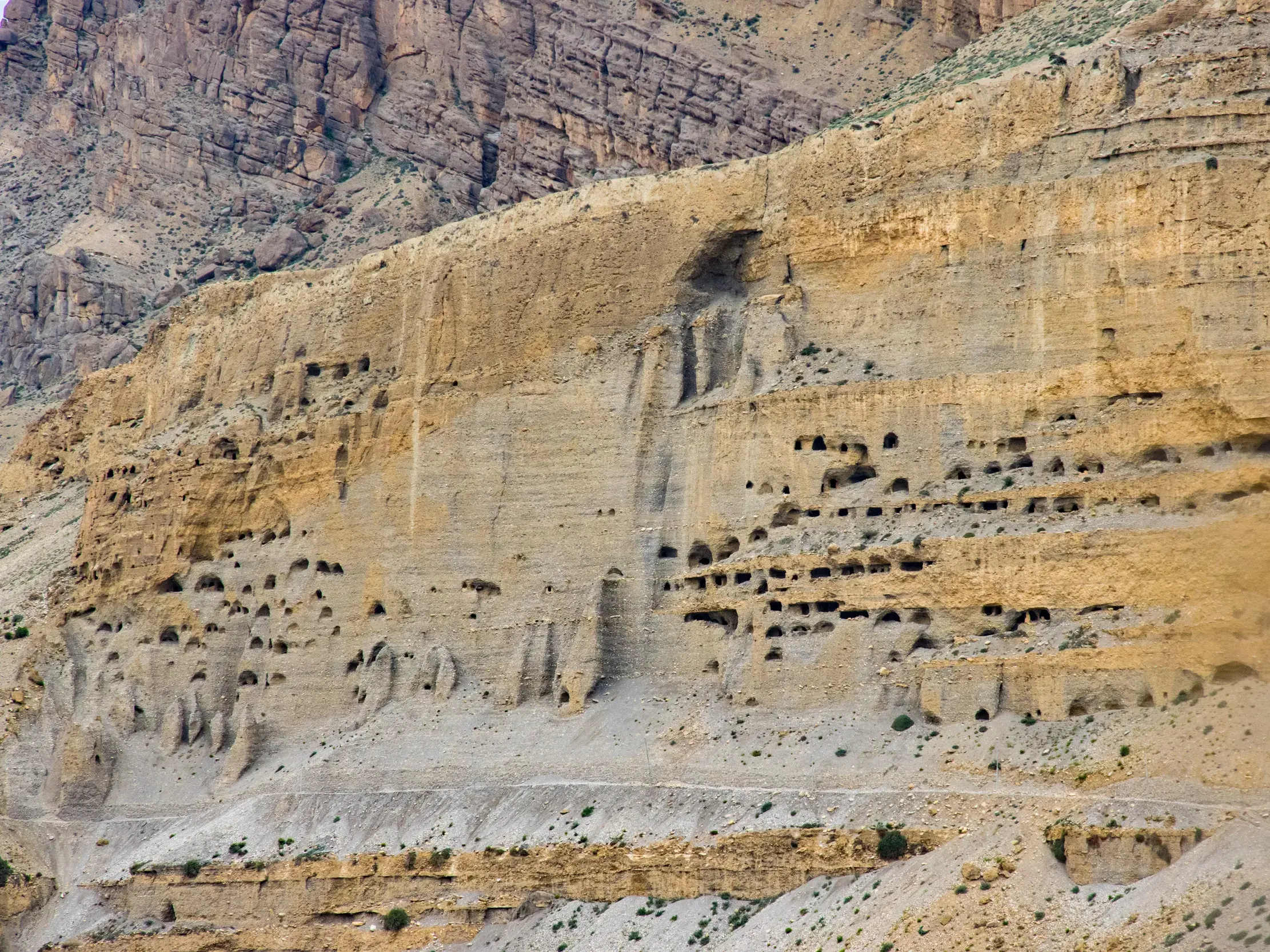 Zahlreiche historische Höhlenwohnungen in einer ockerfarbenen, steilen Felswand während eines Trekkings in Mustang, Nepal.